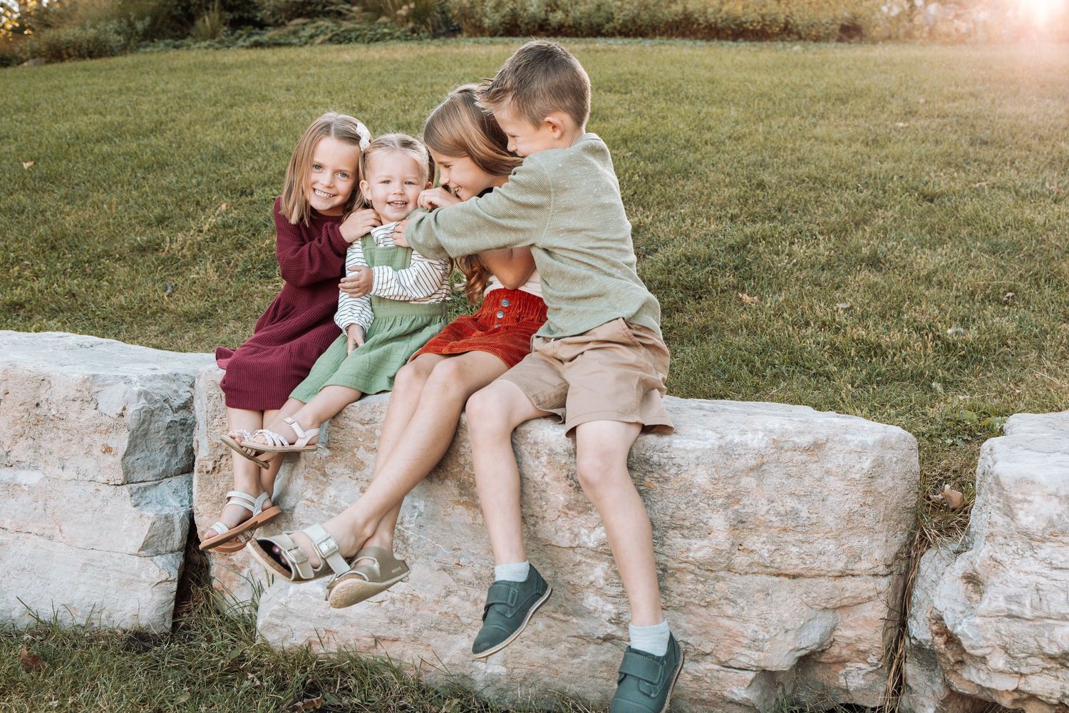 Children sitting together on a stone wall during a warm sunset photo session.