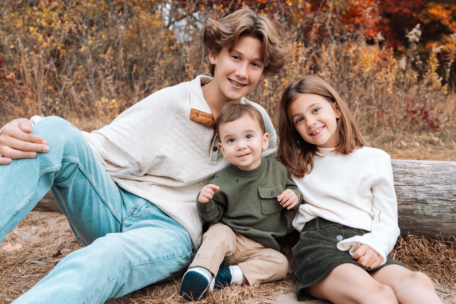 Family lounging together on wooden log during fall photo session.