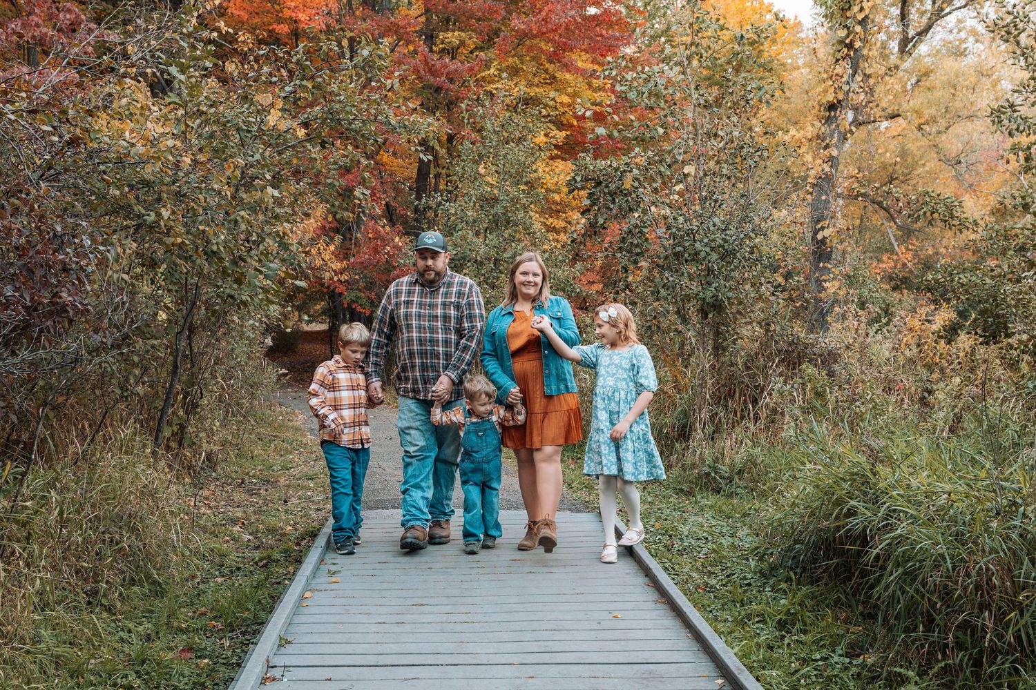 Family walking together on a wooden boardwalk surrounded by vibrant fall colors.