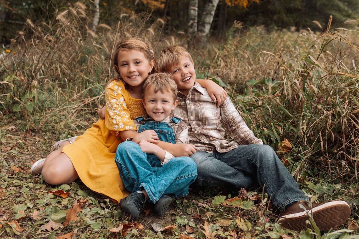 Children lounging in autumn leaves wearing colorful sweaters during outdoor photoshoot.