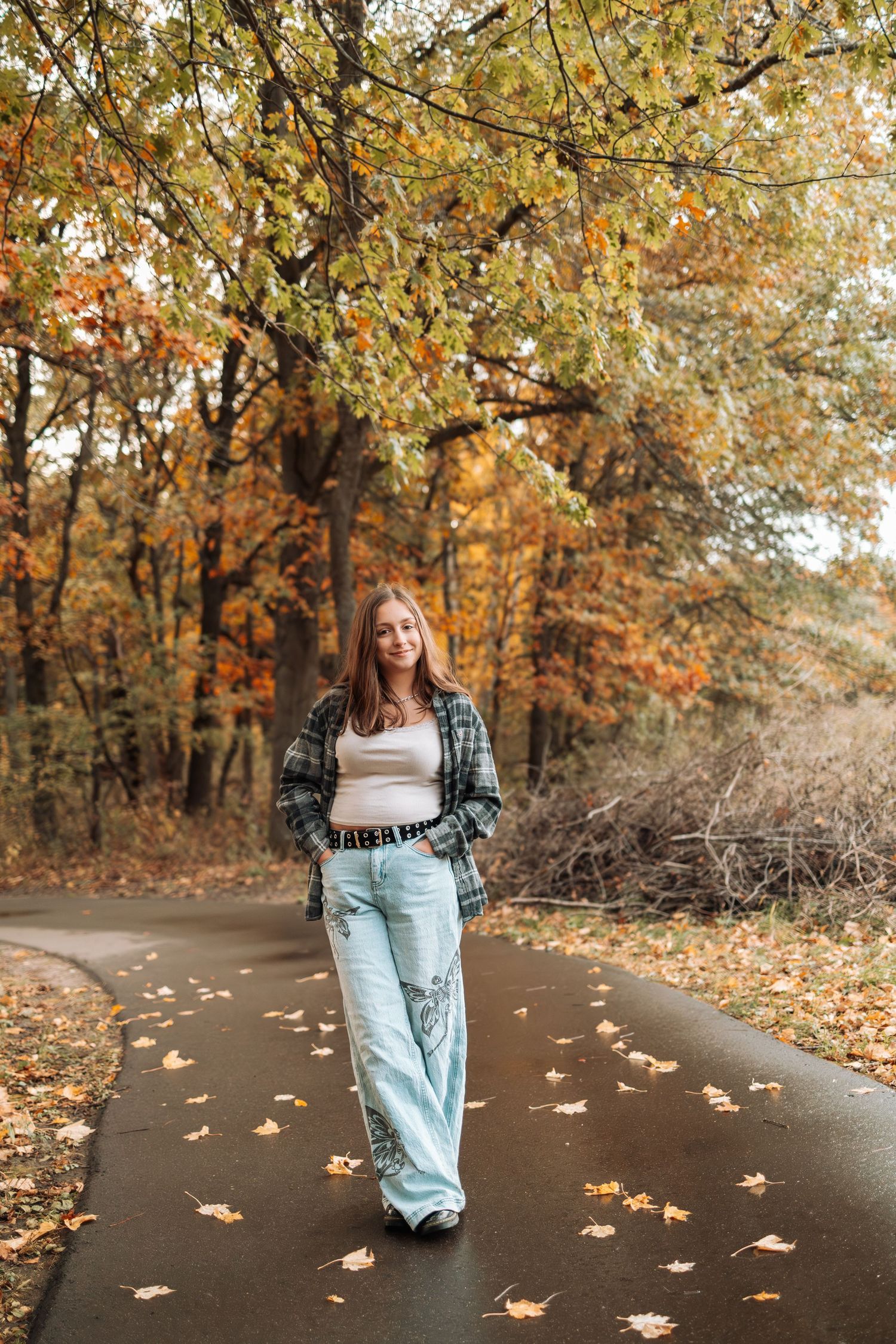 Person in casual outfit walking on path covered with fallen autumn leaves.