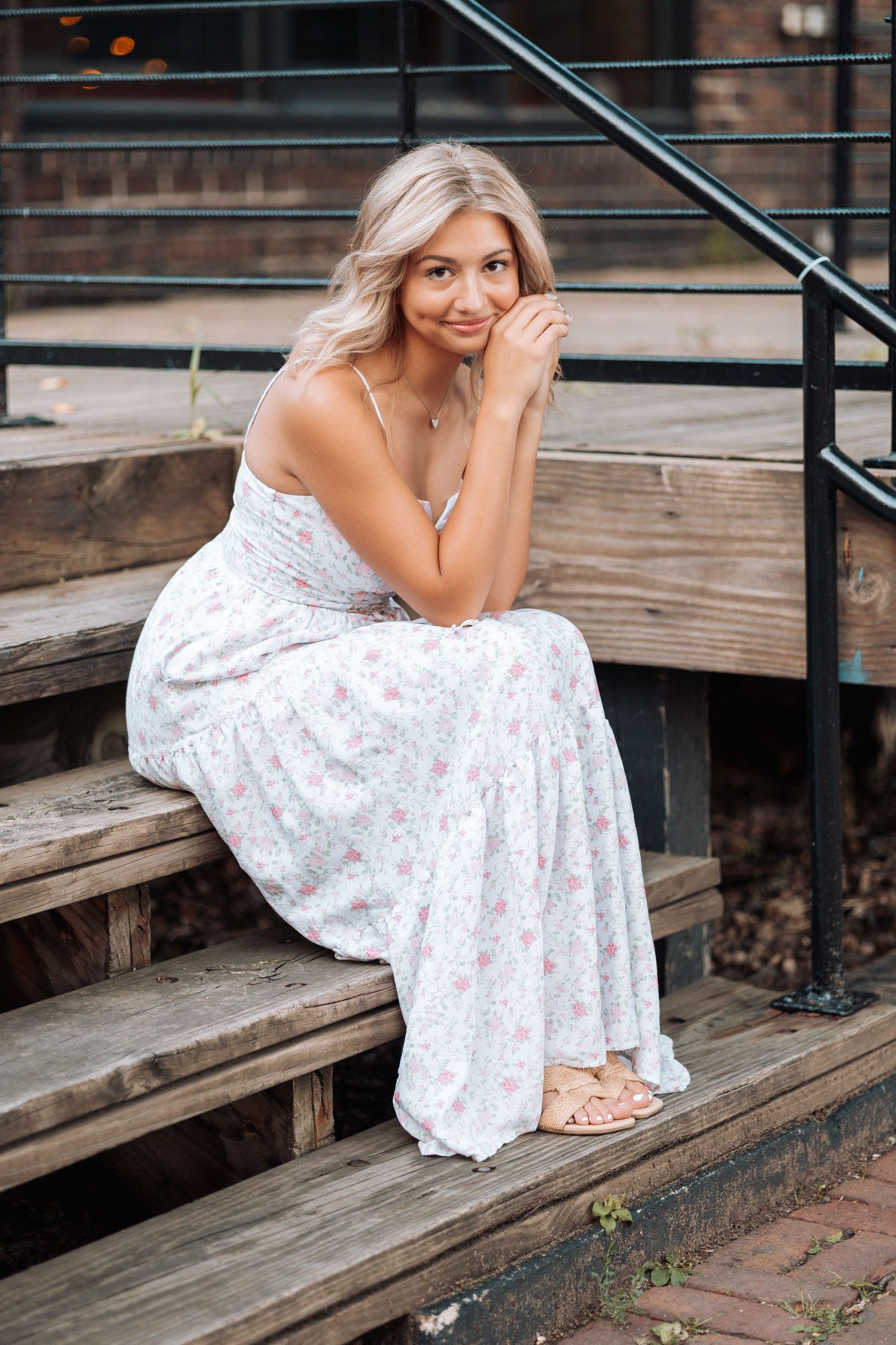Person in white floral maxi dress sitting on wooden steps outdoors with Kenzie Ayla Images in the Twin Cities MN area.
