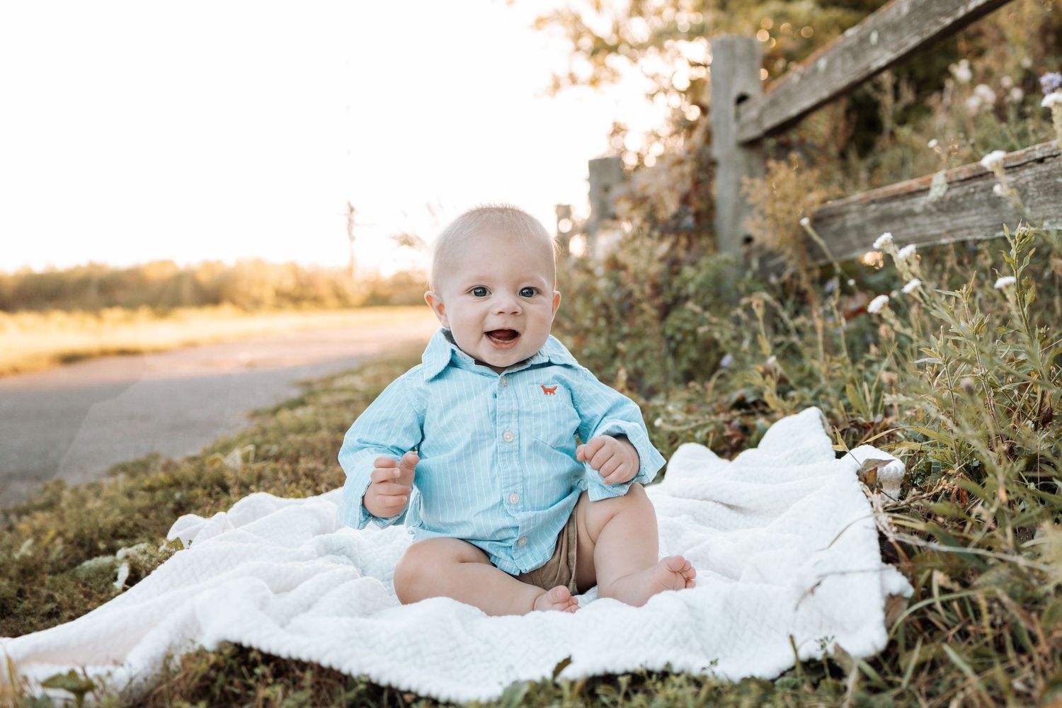 Baby lying on white blanket outdoors during sunset portrait session.