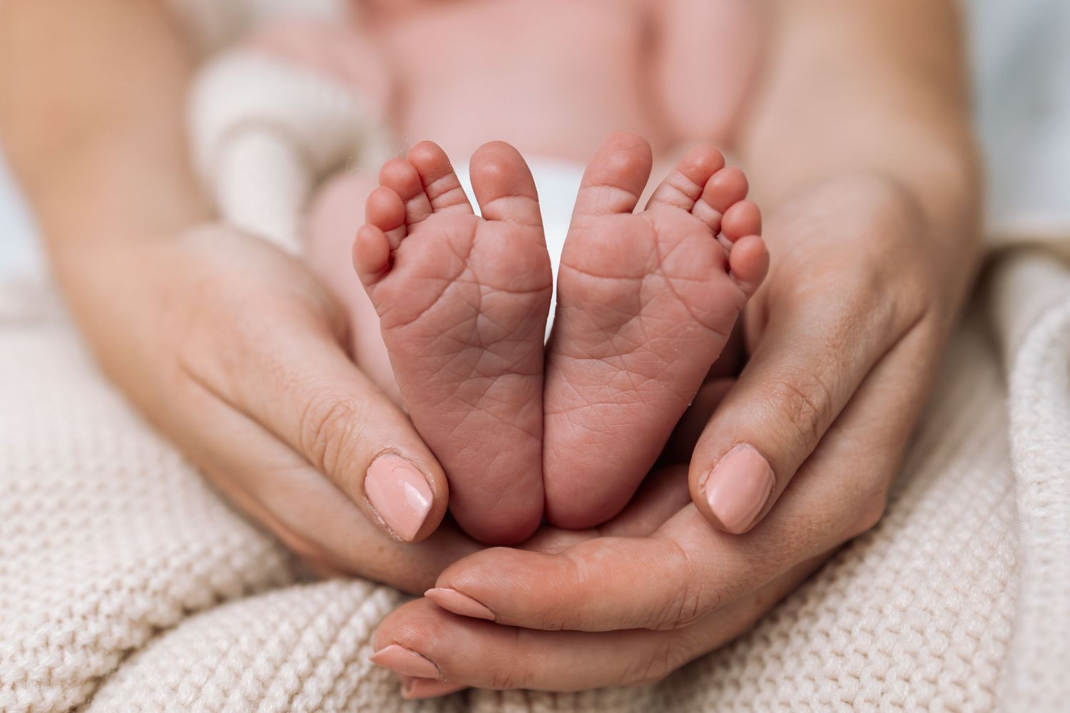 Close-up of tiny baby feet being held by gentle hands on knit blanket.