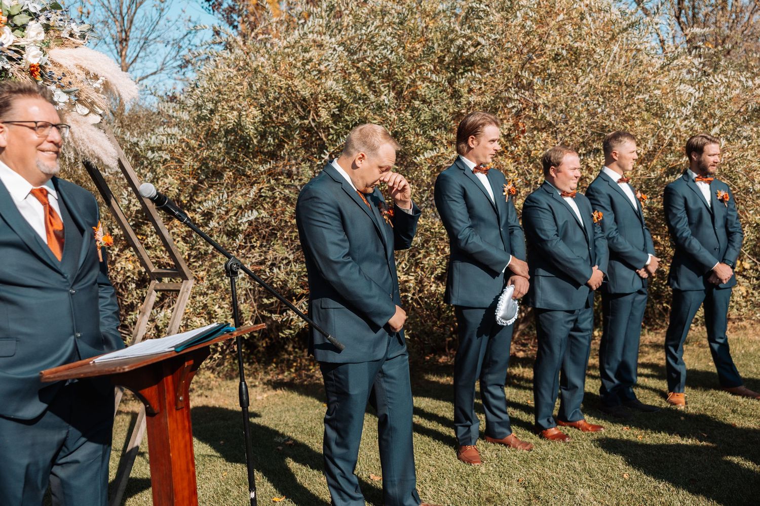 Wedding party and officiant standing at outdoor ceremony with autumn trees in background.