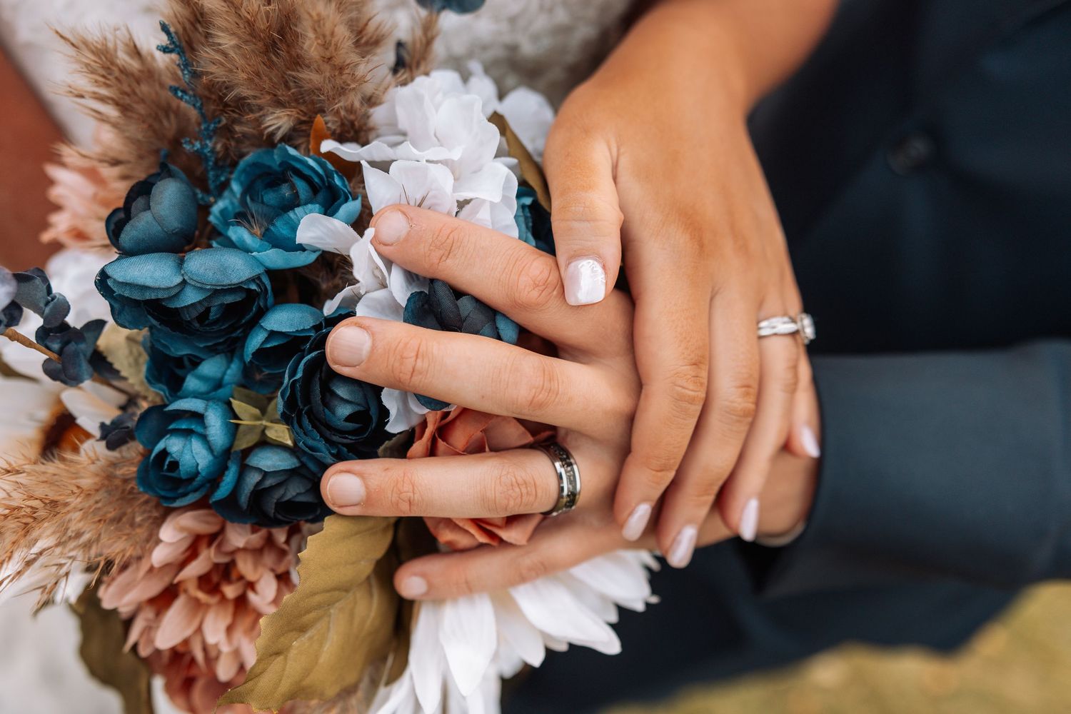 Close-up of hands holding blue and orange autumn wedding bouquet with white flowers.