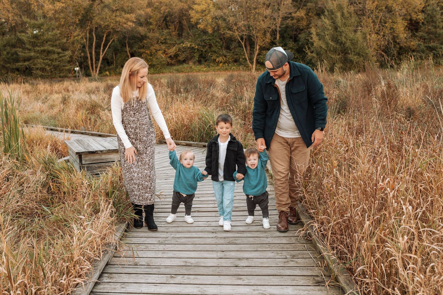 Family walking together on wooden steps surrounded by autumn foliage and tall grasses.