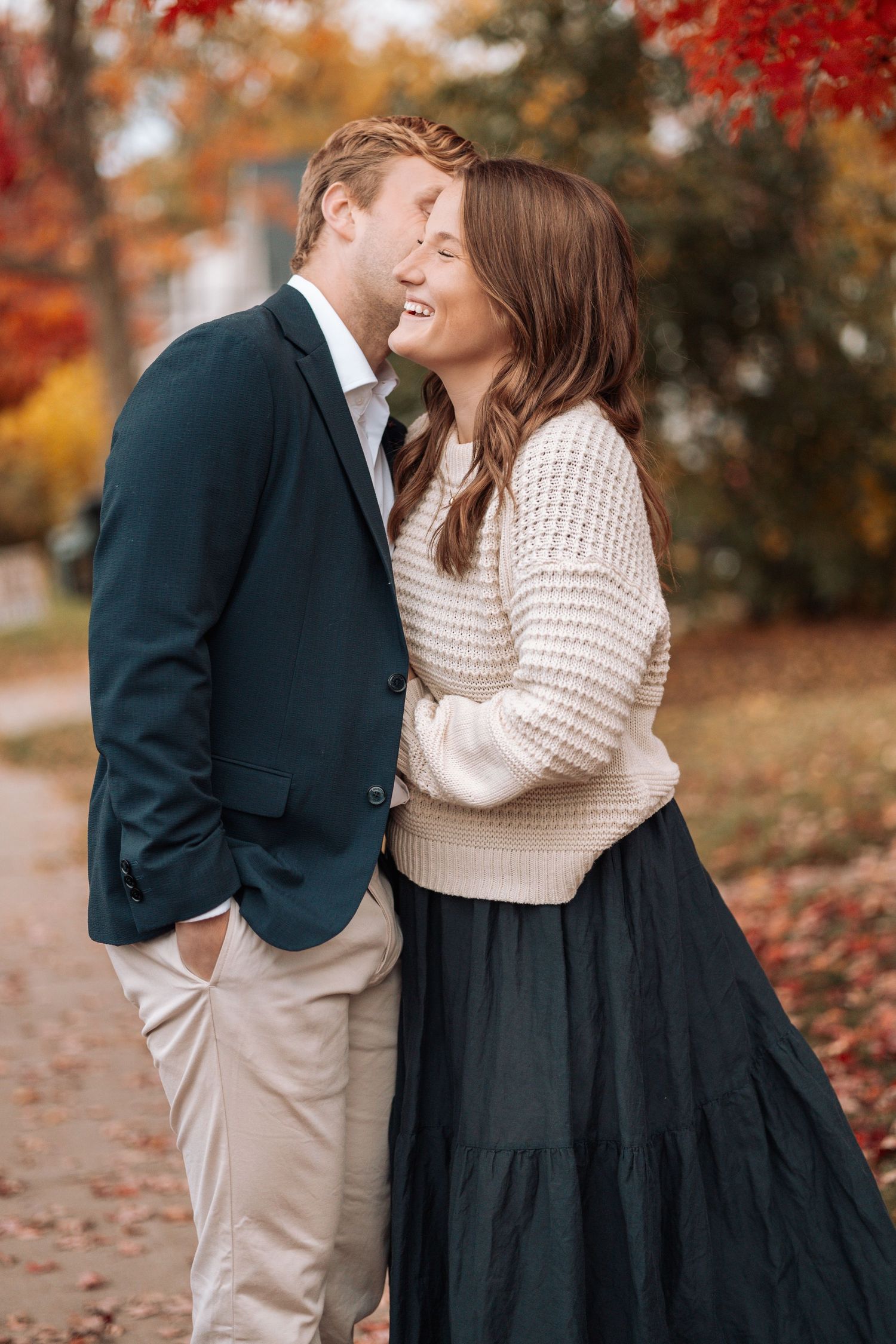 Couple embracing in autumn setting with red maple leaves in background.