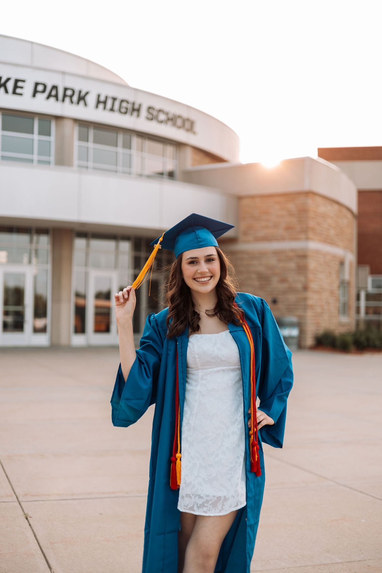 Graduate in blue cap and gown poses outside Spring Lake Park High School at sunset with Kenzie Ayla Images in the Twin Cities MN area.