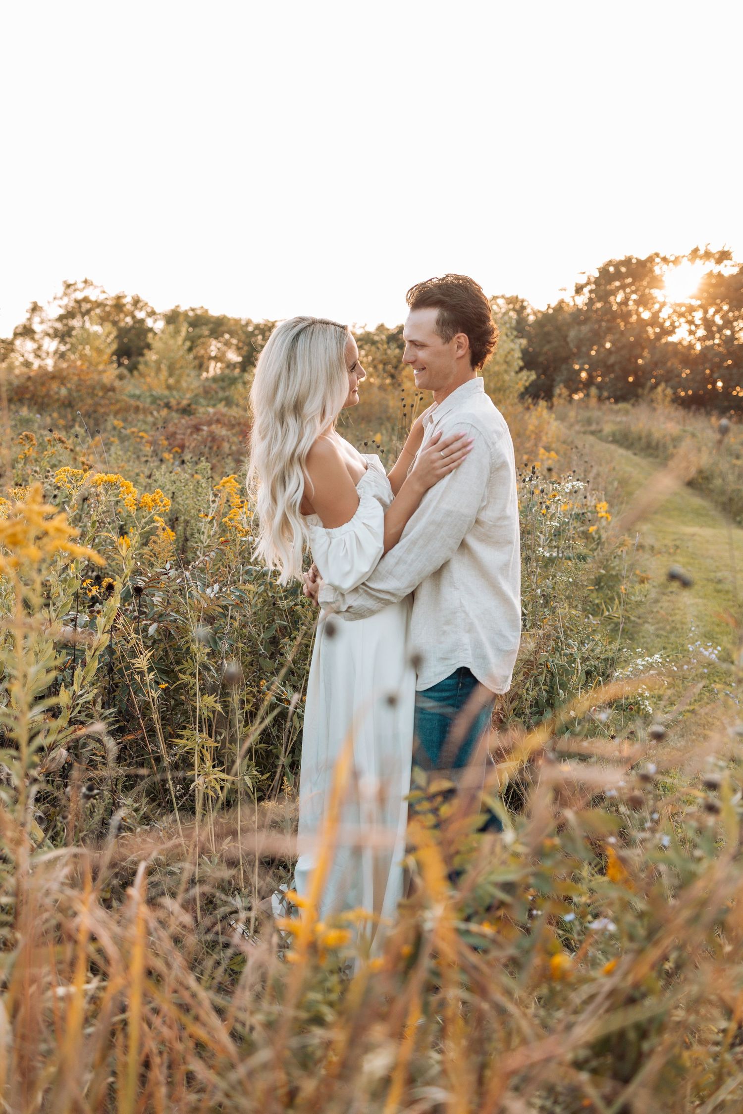 Couple embracing in a wildflower field during golden hour sunset.