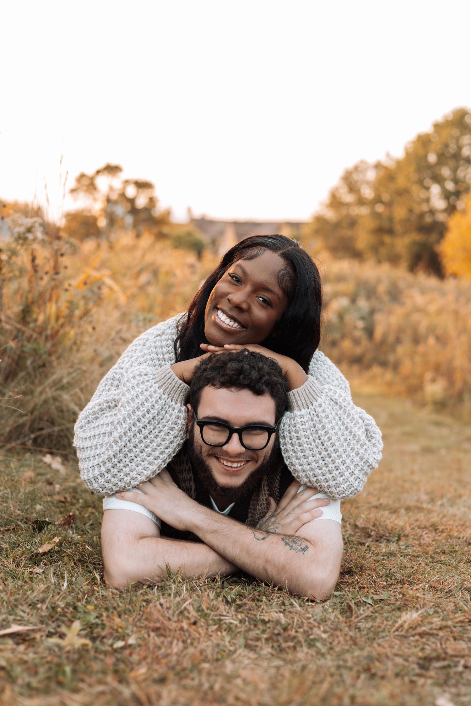 A couple lying in a grassy field during golden hour sharing joyful laughter together.
