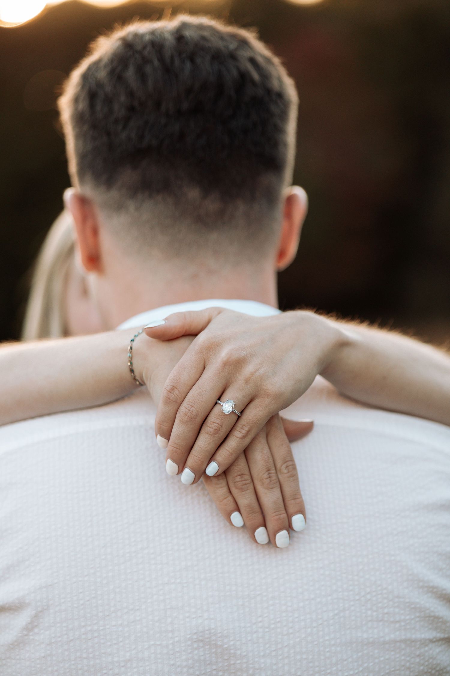 Close-up of hands with engagement ring resting on white shirt.