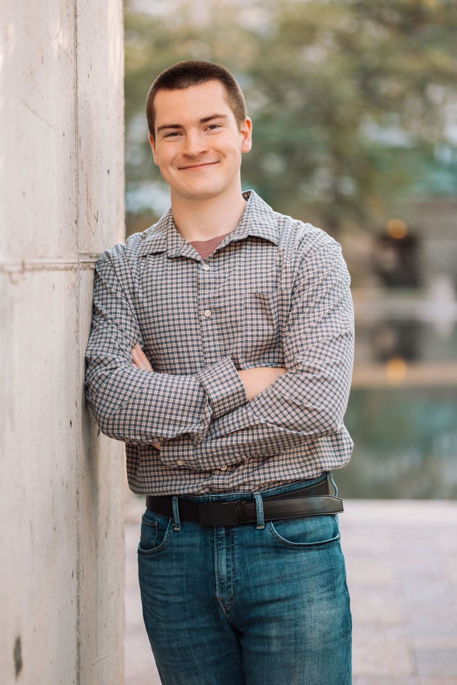 Casual portrait poses against white columns wearing a blue checkered shirt and jeans.