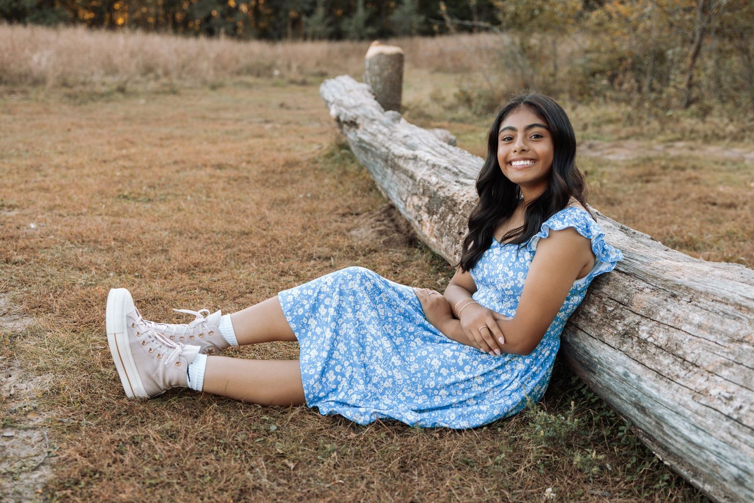 A person in a blue floral dress lounges casually on a fallen tree trunk in a natural outdoor setting.