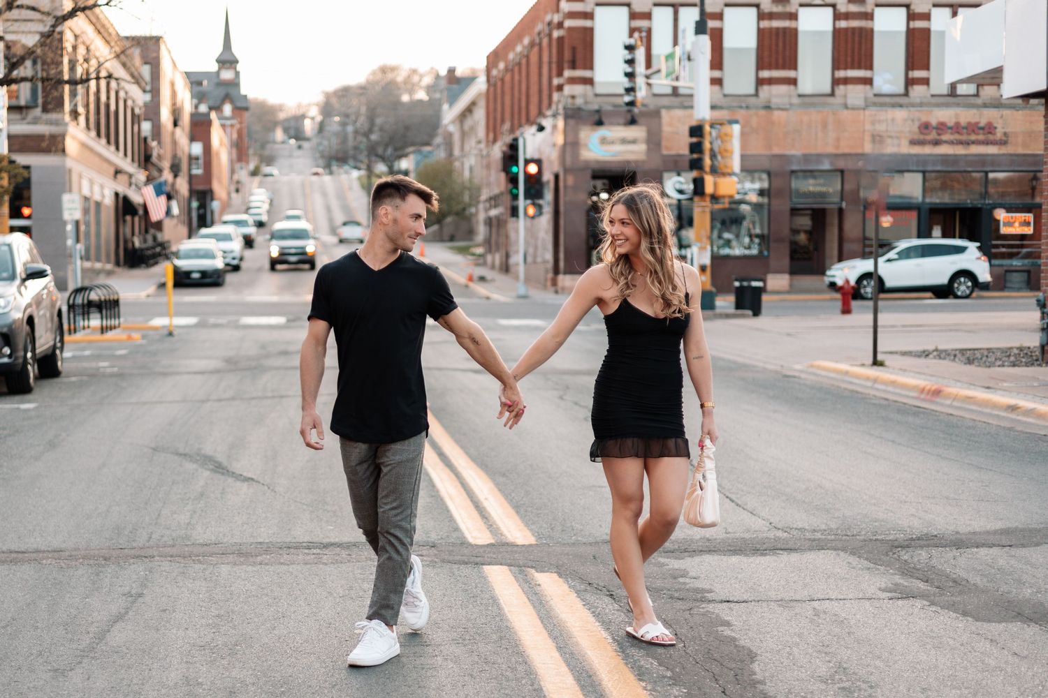 Couple walking hand in hand down urban street with brick buildings.