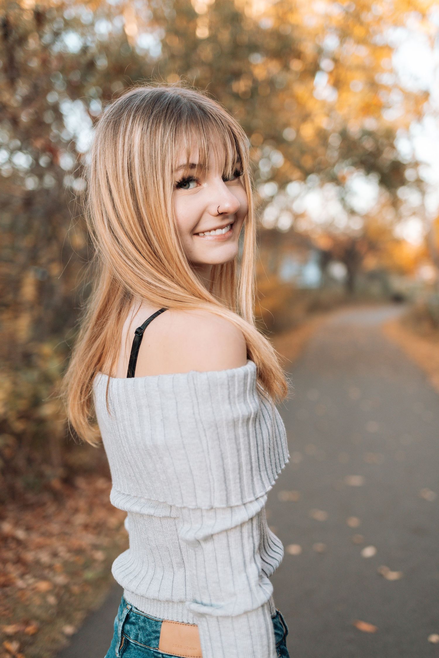 Woman in white sweater smiles over shoulder on autumn path with Kenzie Ayla Images in the Twin Cities MN area.