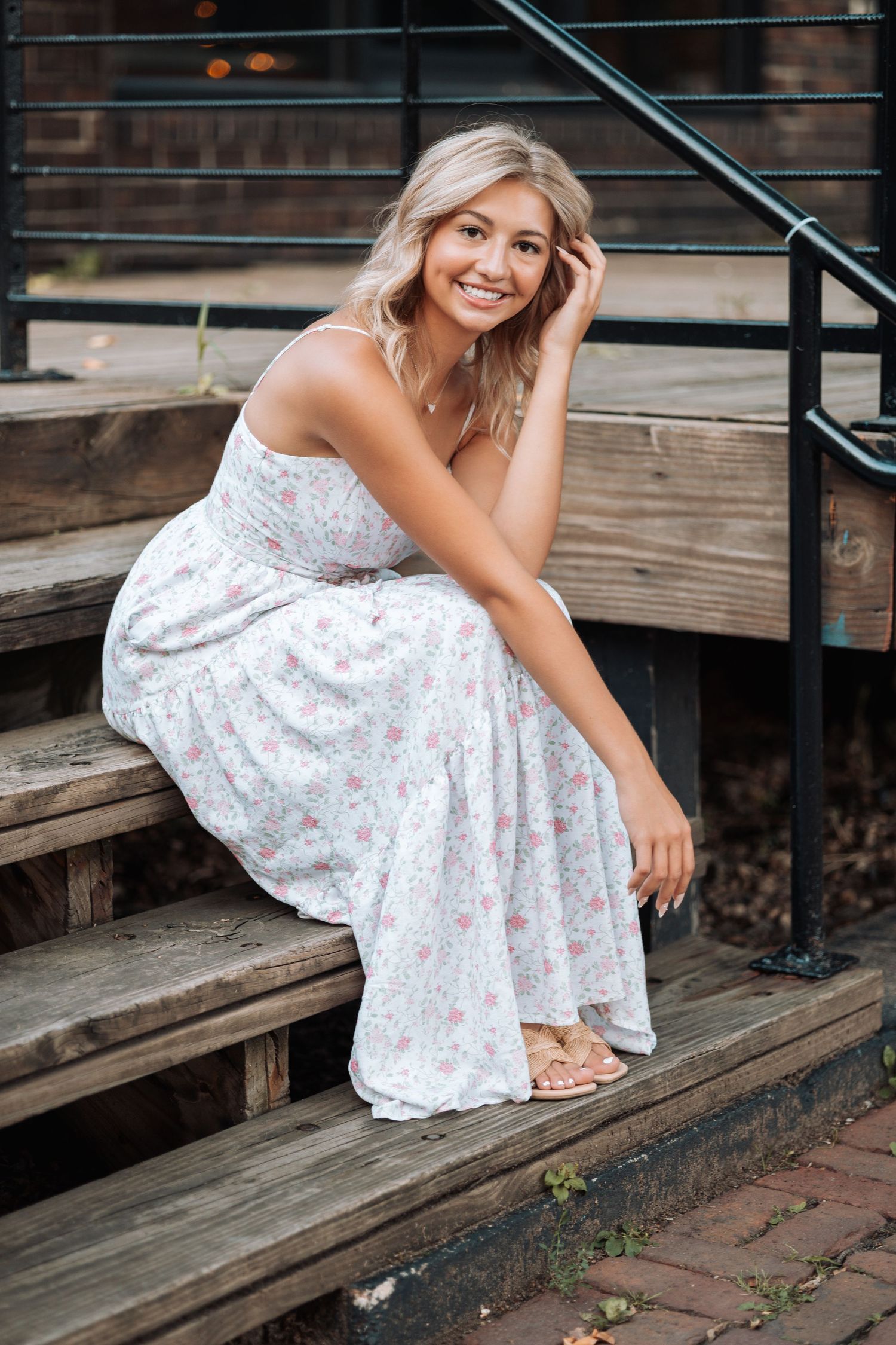 Person in floral dress posing on wooden steps outdoors.