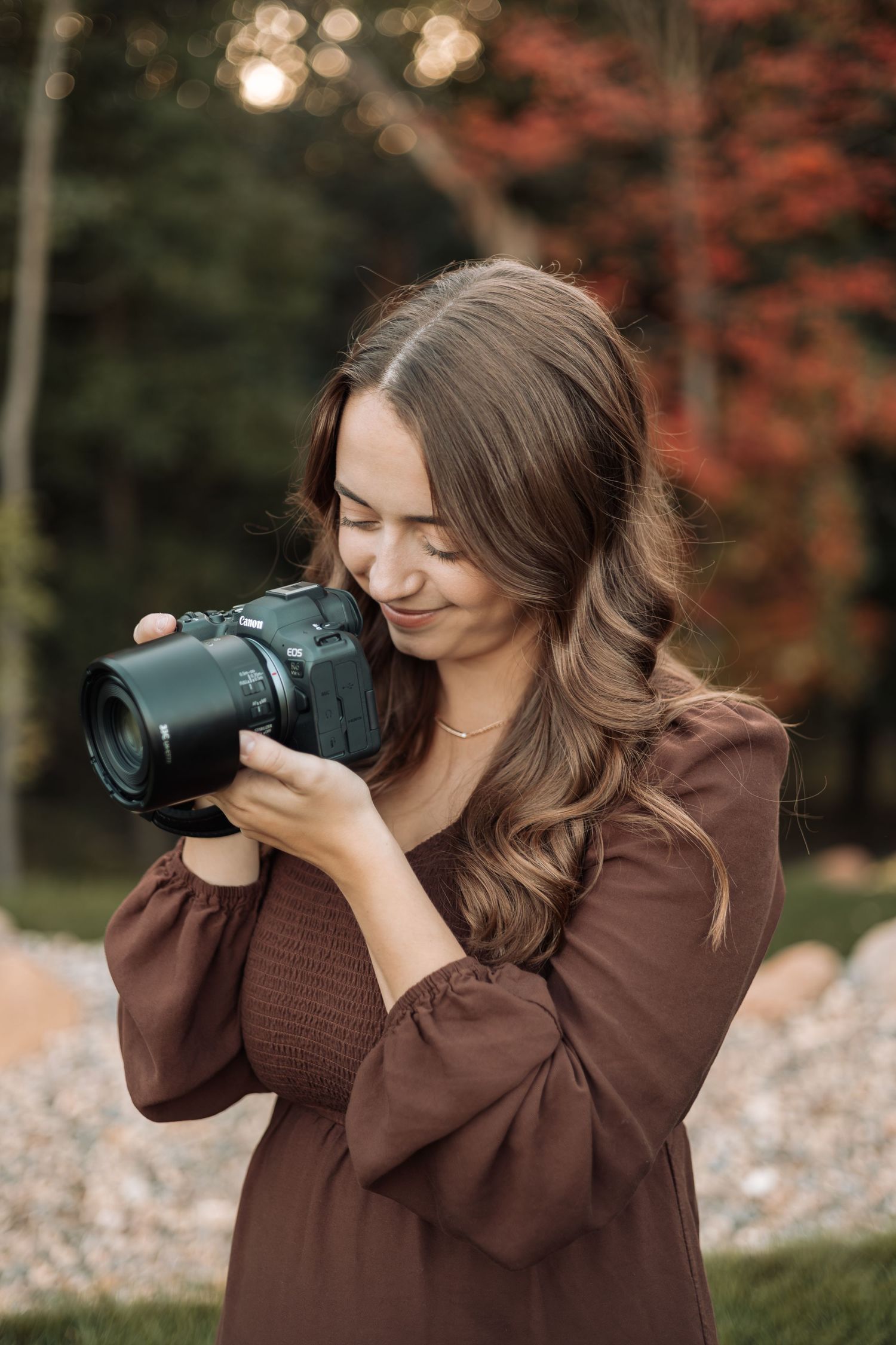 Photographer wearing brown sweater takes photos in autumn setting with red foliage.