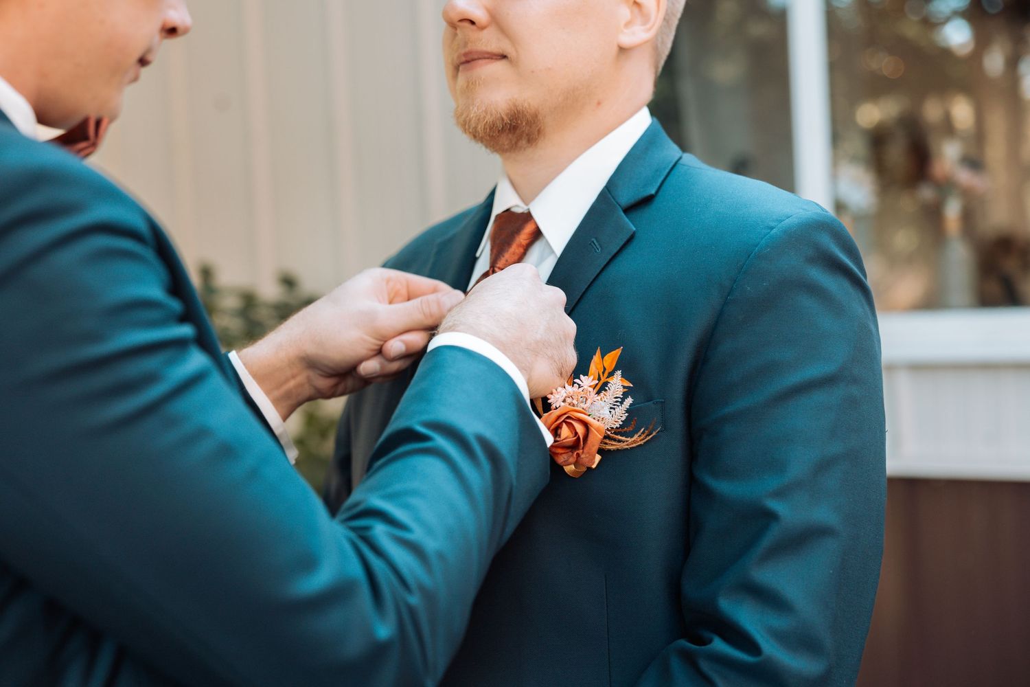 Close-up of boutonniere being pinned to teal suit jacket.