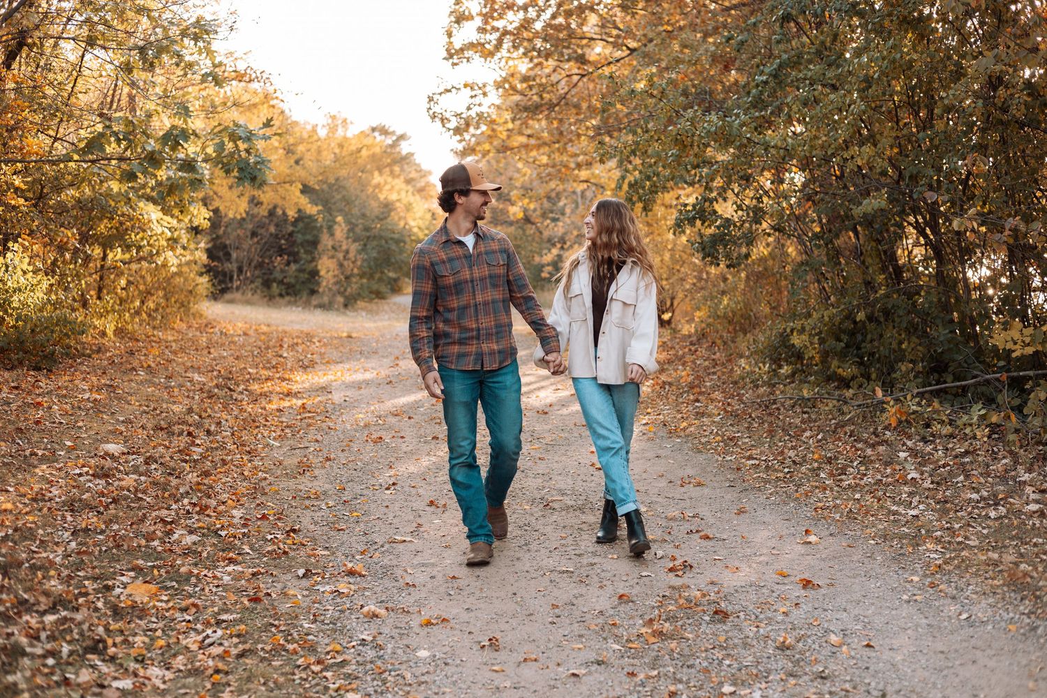 Couple walking hand in hand on leaf-covered path in autumn.