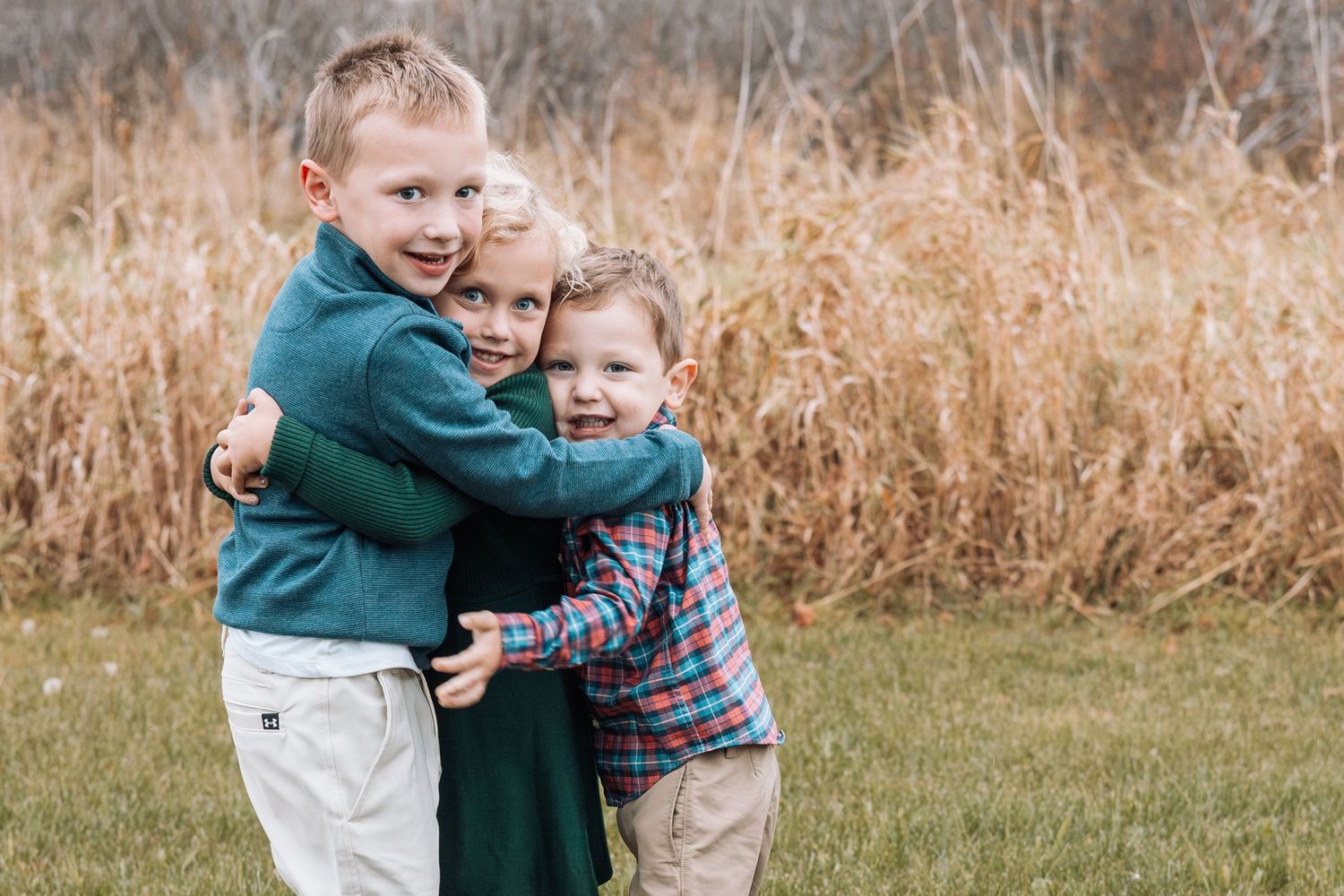 Family shares loving embraces in a field of tall autumn grass during outdoor photo session.