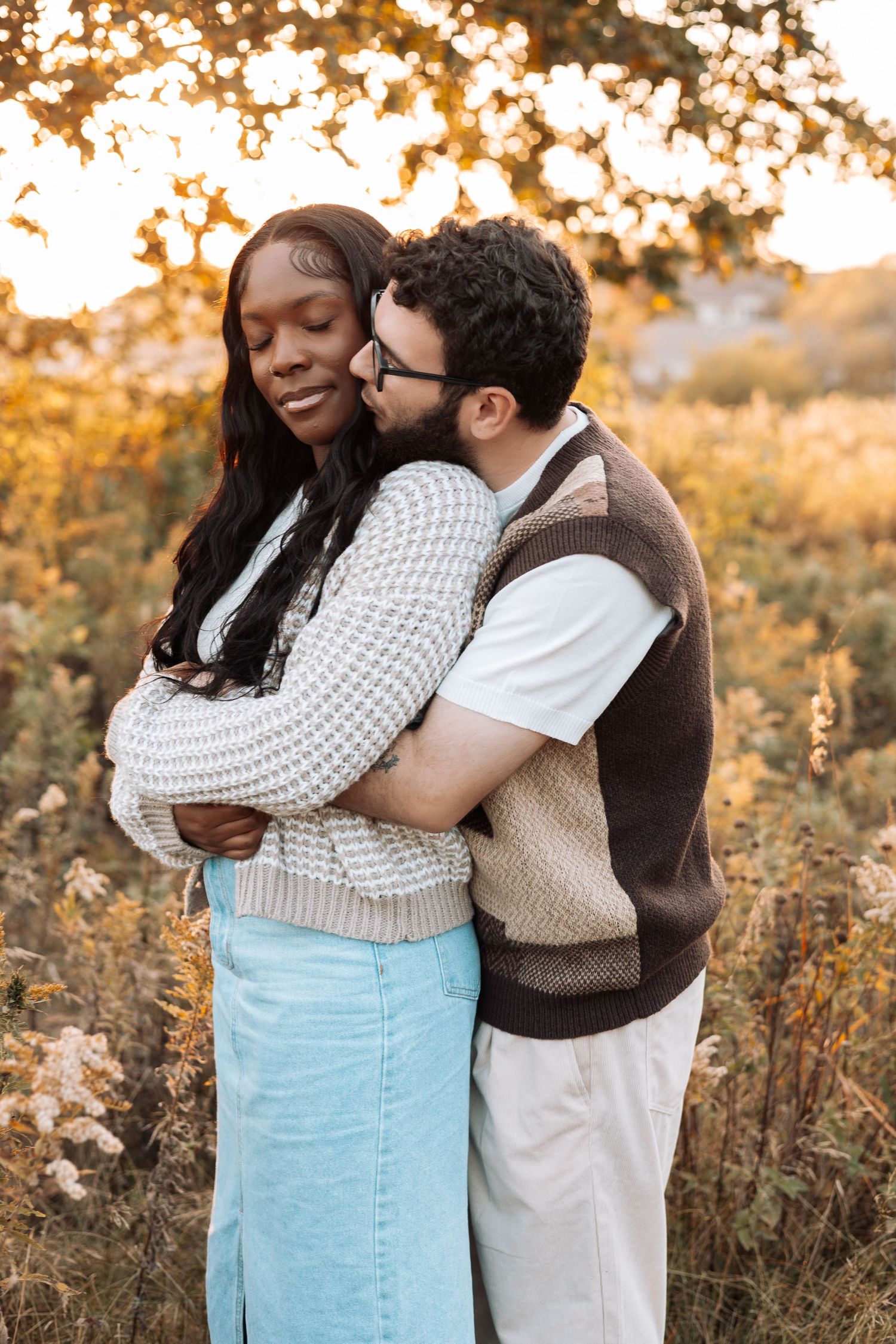 Couple sharing warm embrace in autumn field during sunset.