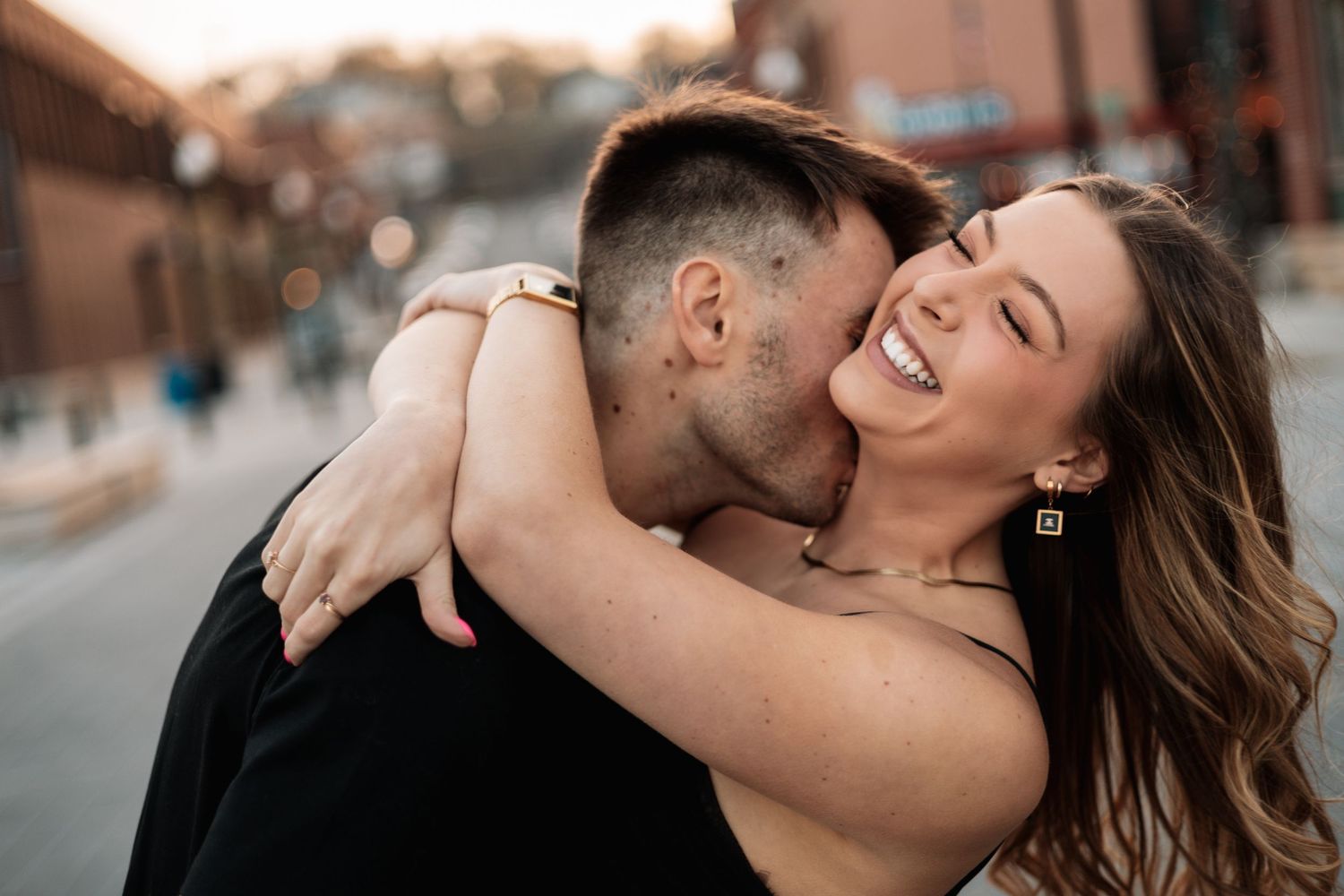 Couple sharing a playful embrace and laugh on urban street at dusk.