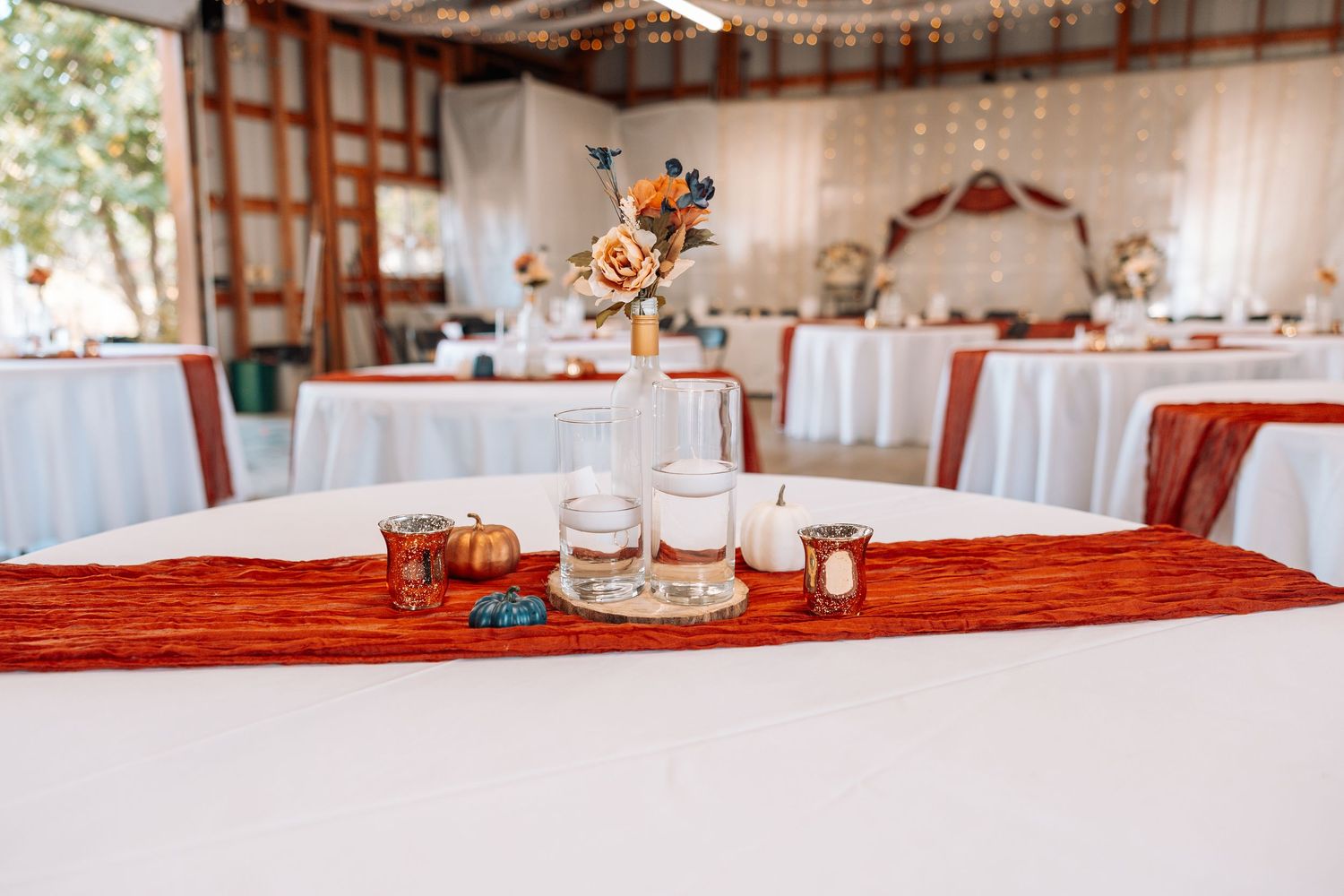 Wedding reception table with rustic decor featuring an orange runner and floating centerpiece arrangement.