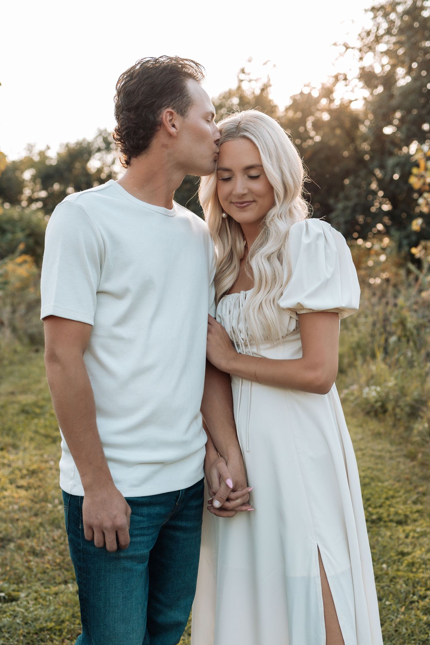 A couple in white outfits sharing an intimate moment in a sunlit field.