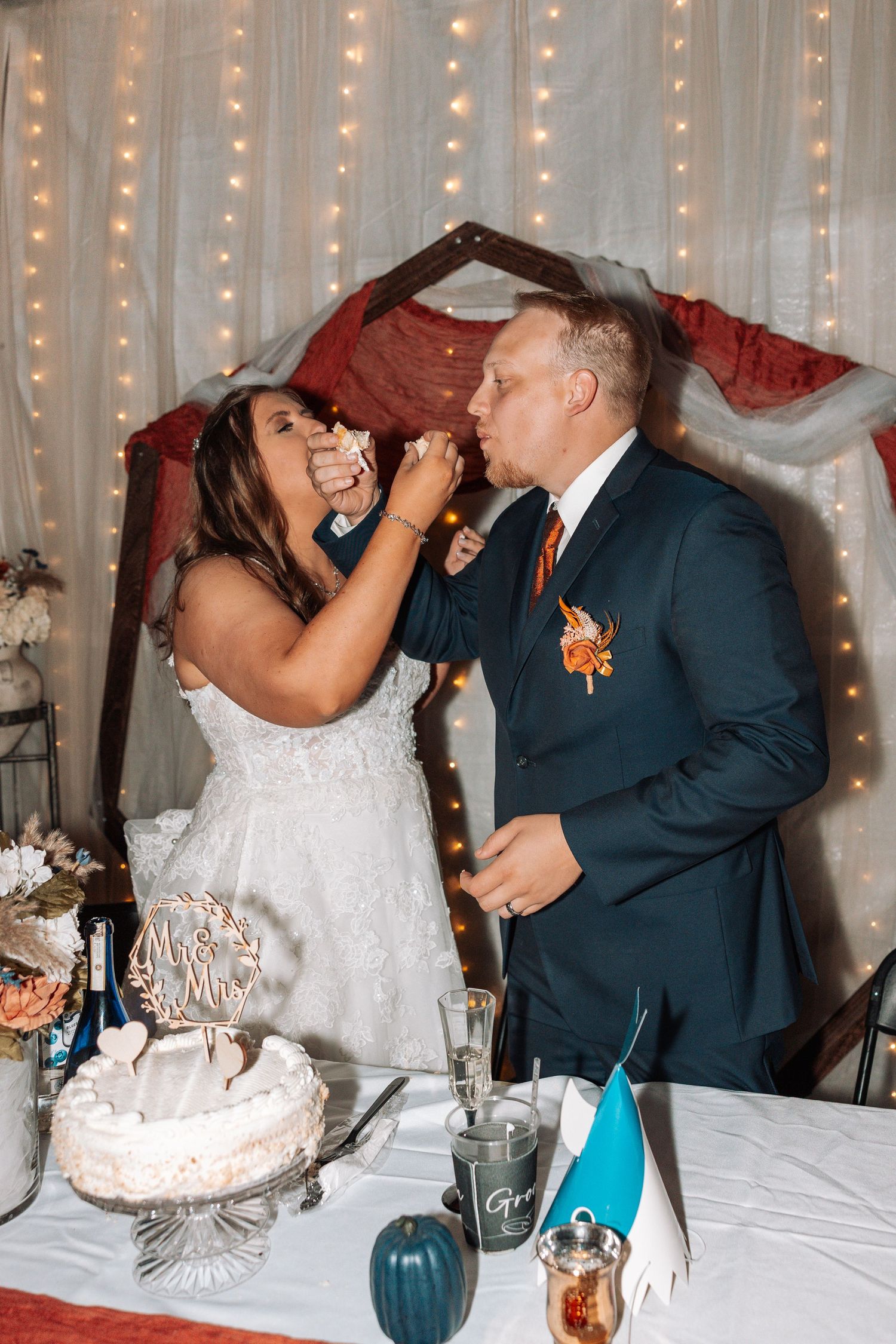 Wedding cake cutting moment with string lights and decorative table settings in the background.