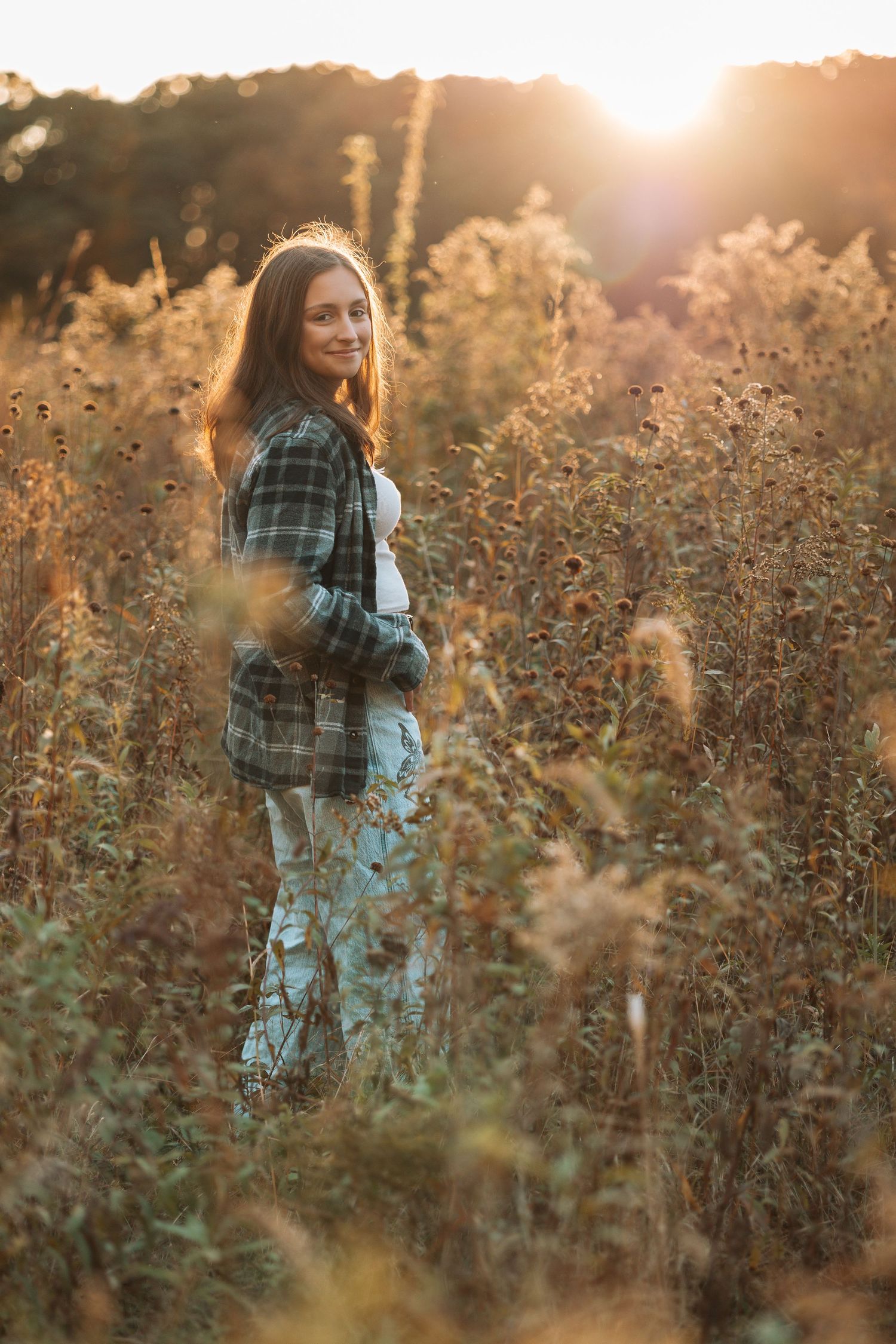Person in plaid shirt walking through golden field at sunset.