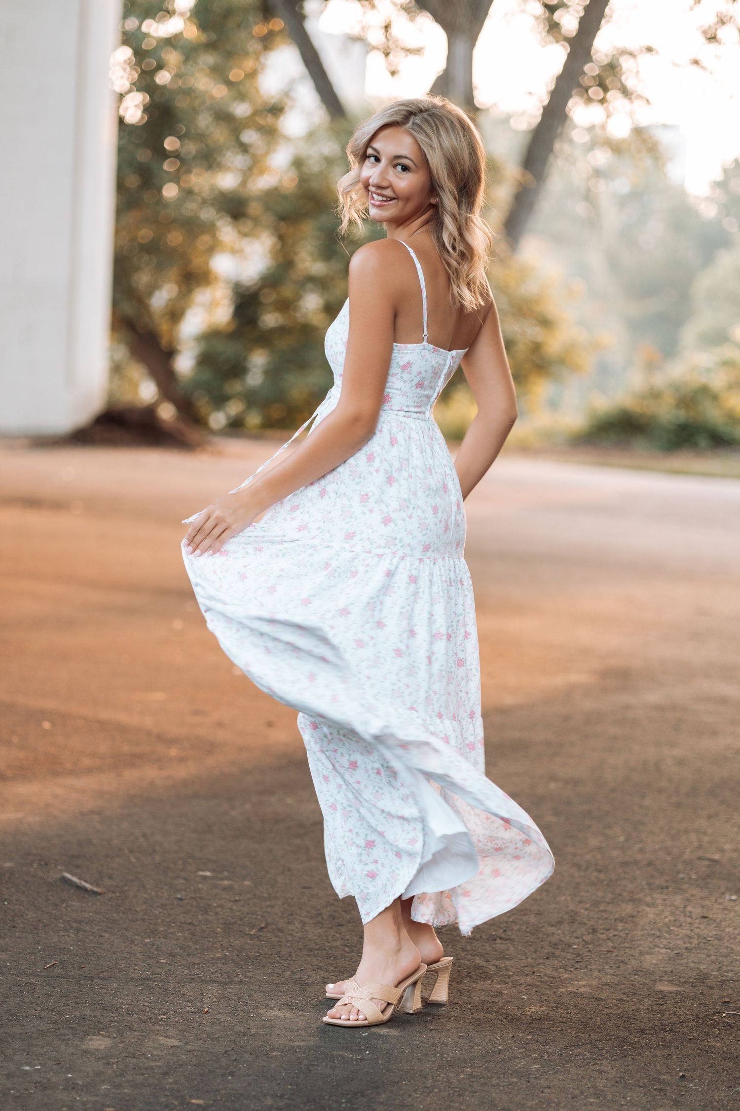 Person in flowing white floral dress twirling on a pathway at sunset with Kenzie Ayla Images in the Twin Cities MN area.