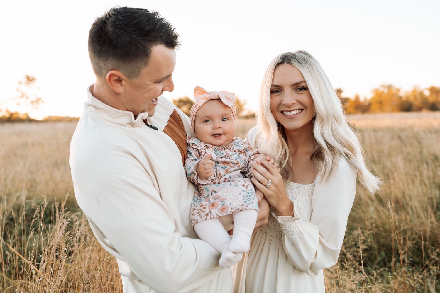Family wearing white clothing shares joyful moments in a golden field at sunset.