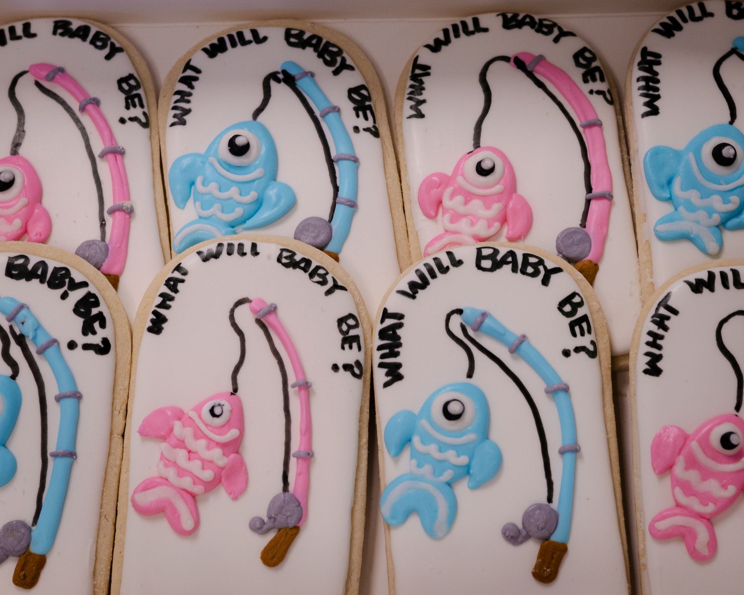 Decorated sugar cookies with fishing theme reading What Will Baby Be in pink and blue.
