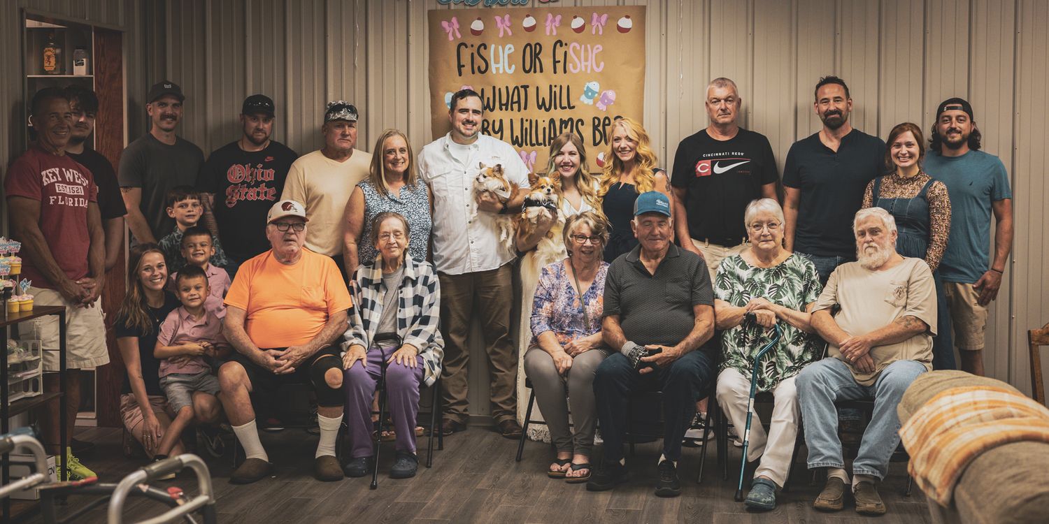 Large family group photo at a fishing-themed gender reveal party indoors.