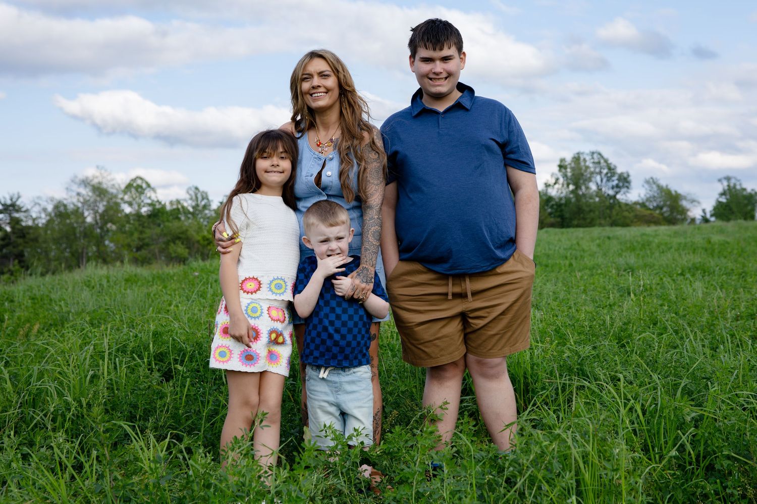 Happy family of four posing together in a lush green meadow on a sunny day.