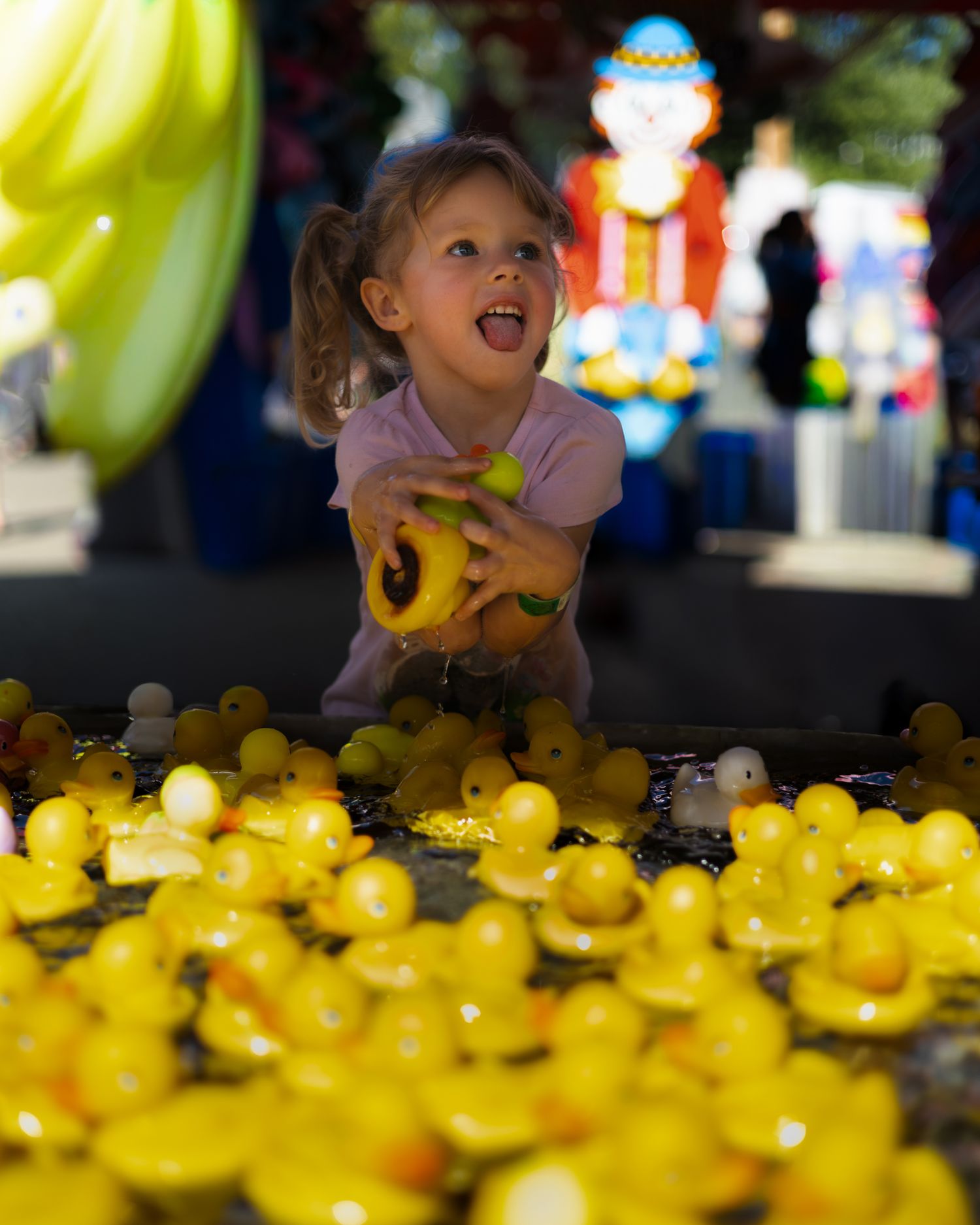 Excited young girl reaching for yellow rubber ducks at a carnival game booth.
