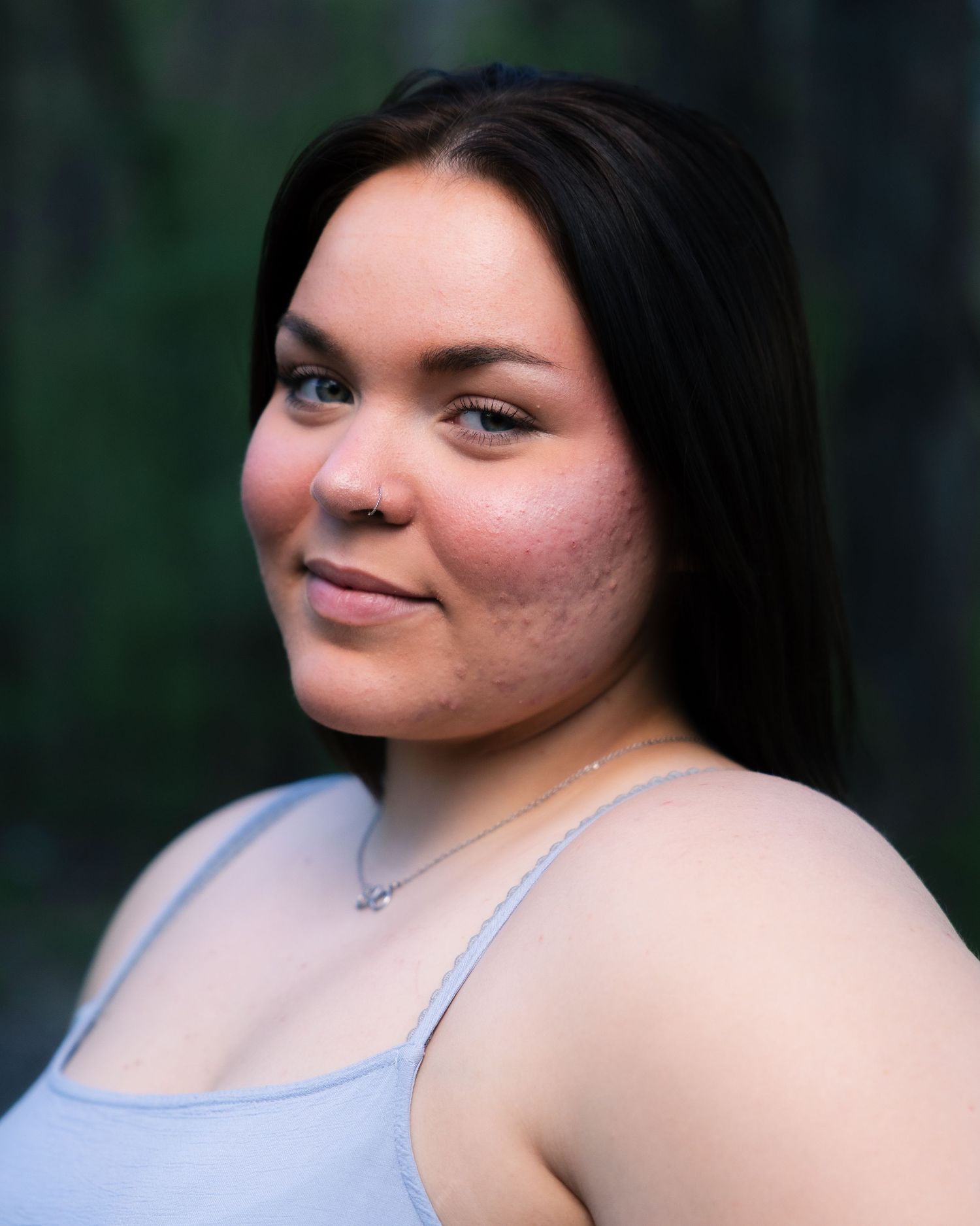 Young woman with long black hair and natural skin smiles softly in outdoor portrait session.