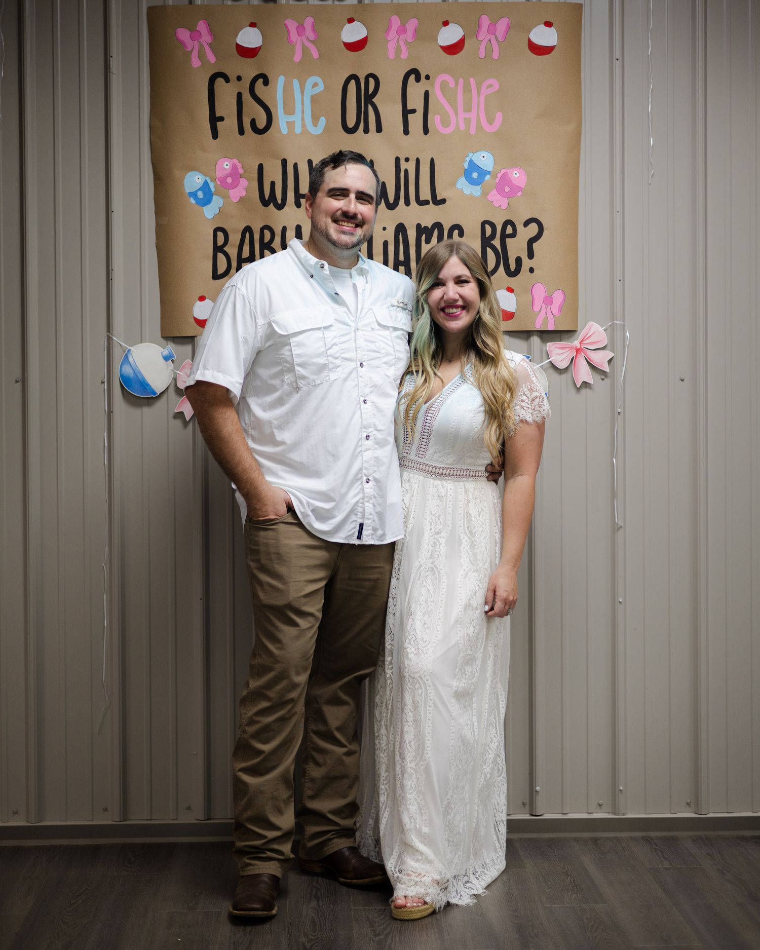 Couple posing in front of Fisher or Fishe What Will Baby Williams Be gender reveal banner.