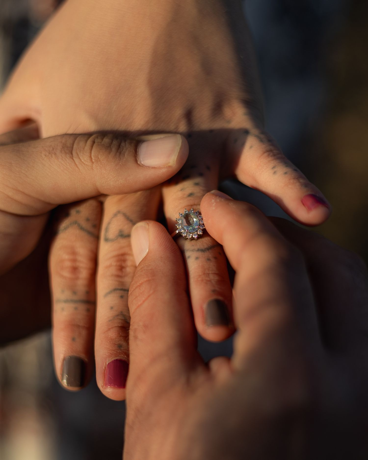 Close-up of tattooed hands with diamond engagement ring during romantic proposal moment.