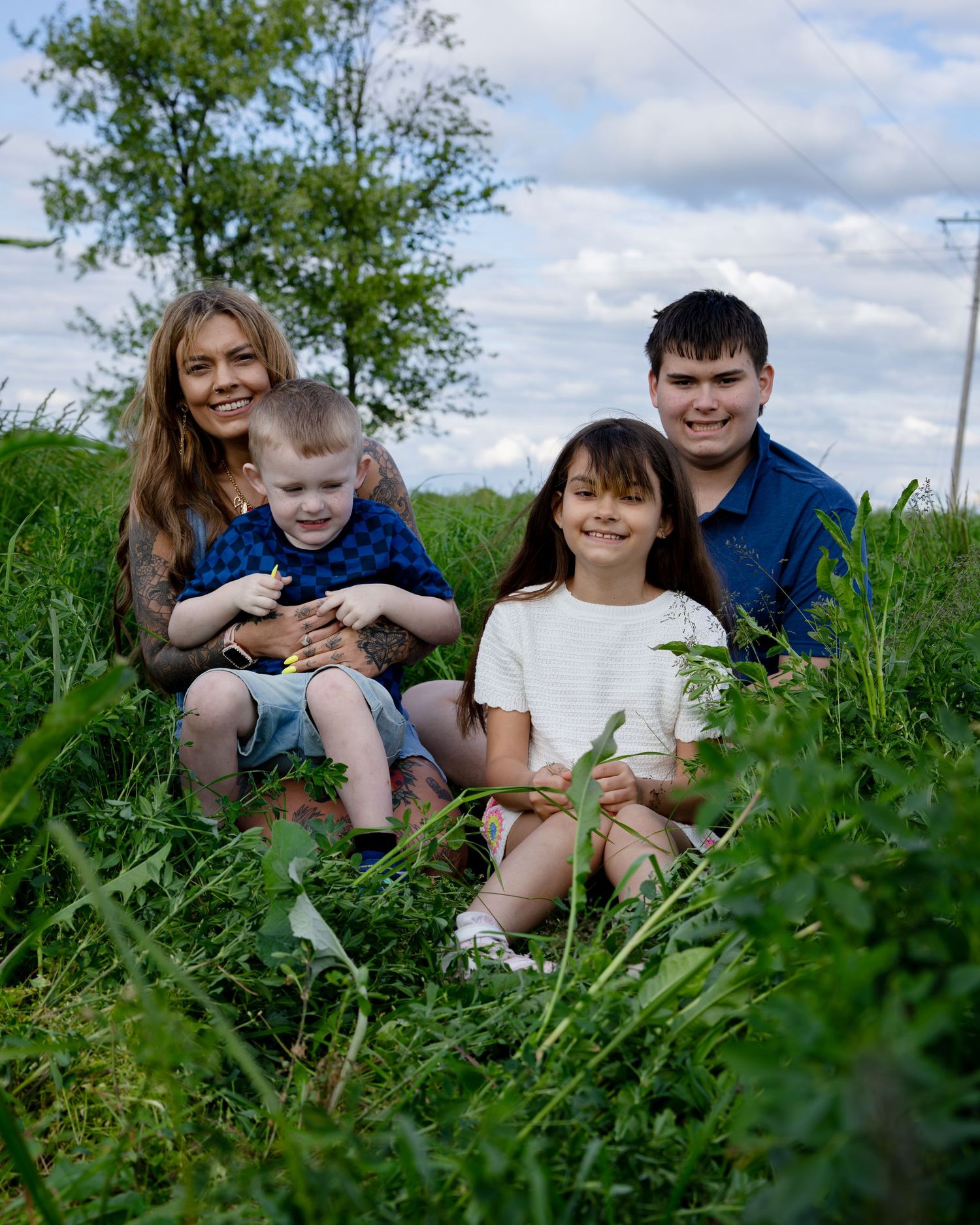 Family of four smiling together in a lush green field on a cloudy day, with two adults and two children.
