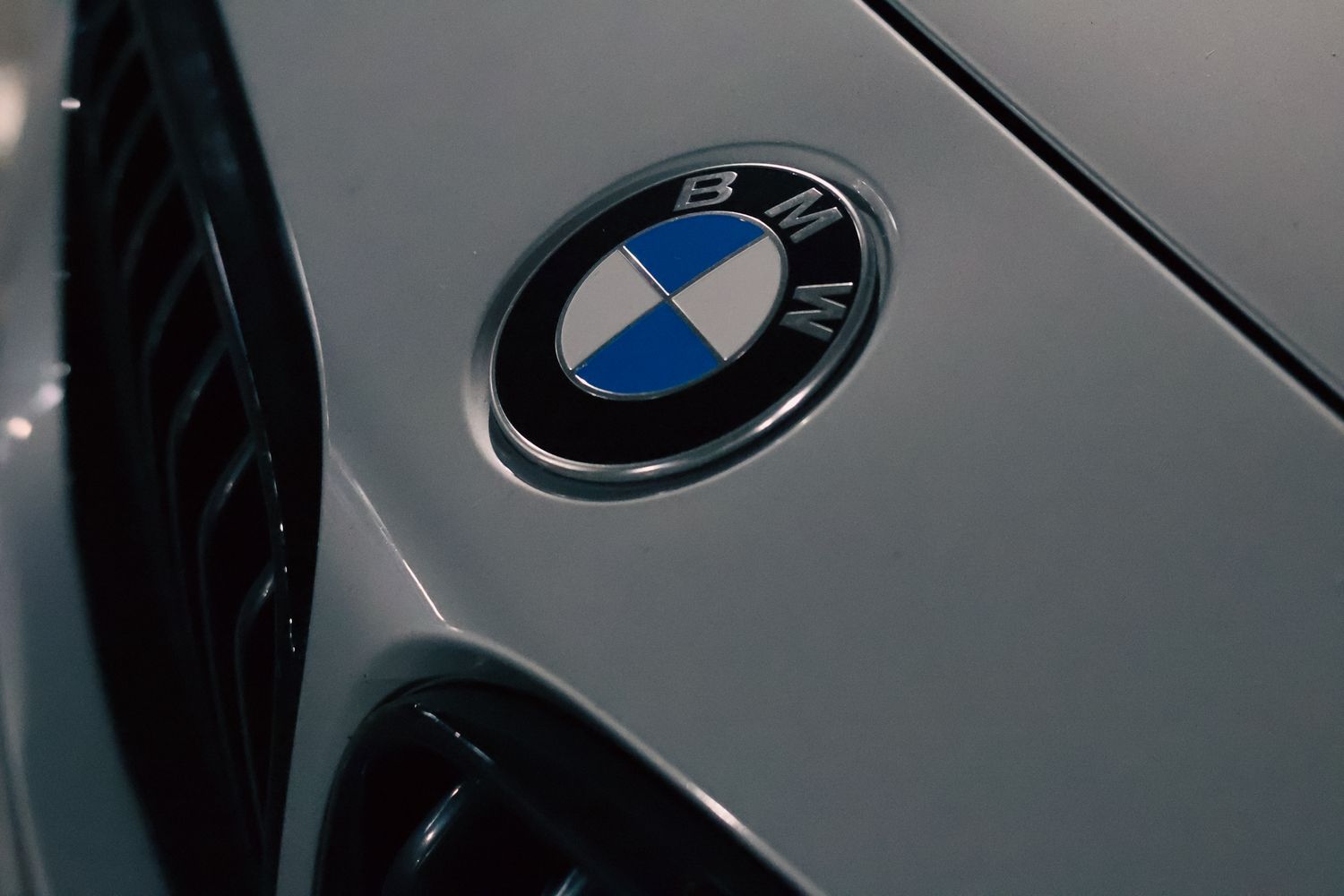 Close-up of iconic BMW roundel logo badge on silver car hood showing blue and white emblem.