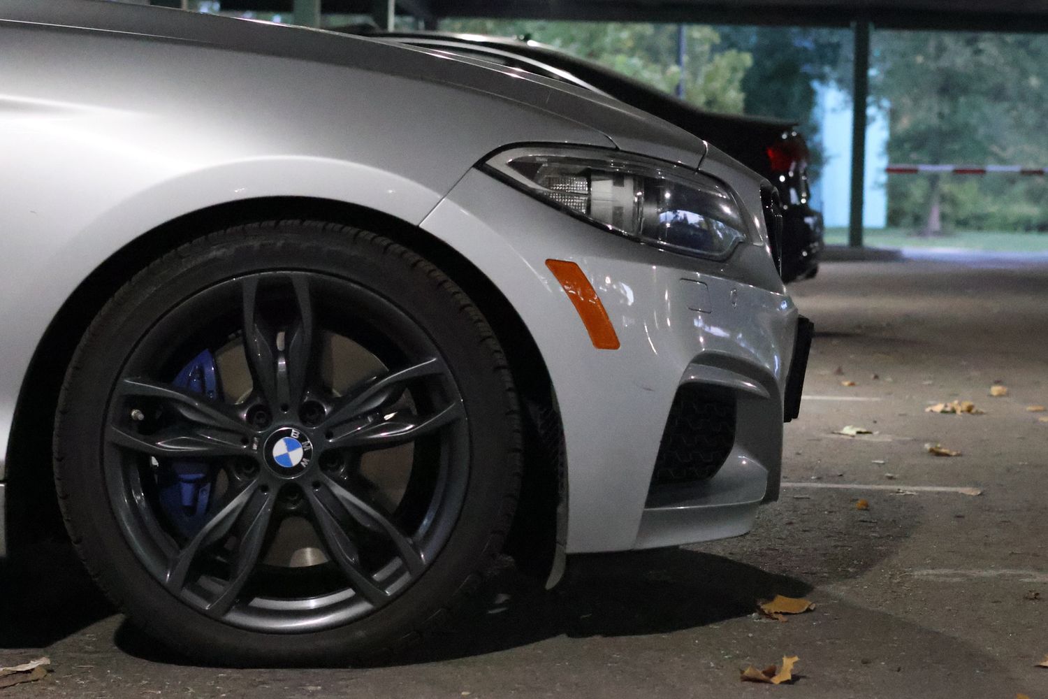 Silver BMW sports car close-up showing blue brake calipers and M-series alloy wheel at night.