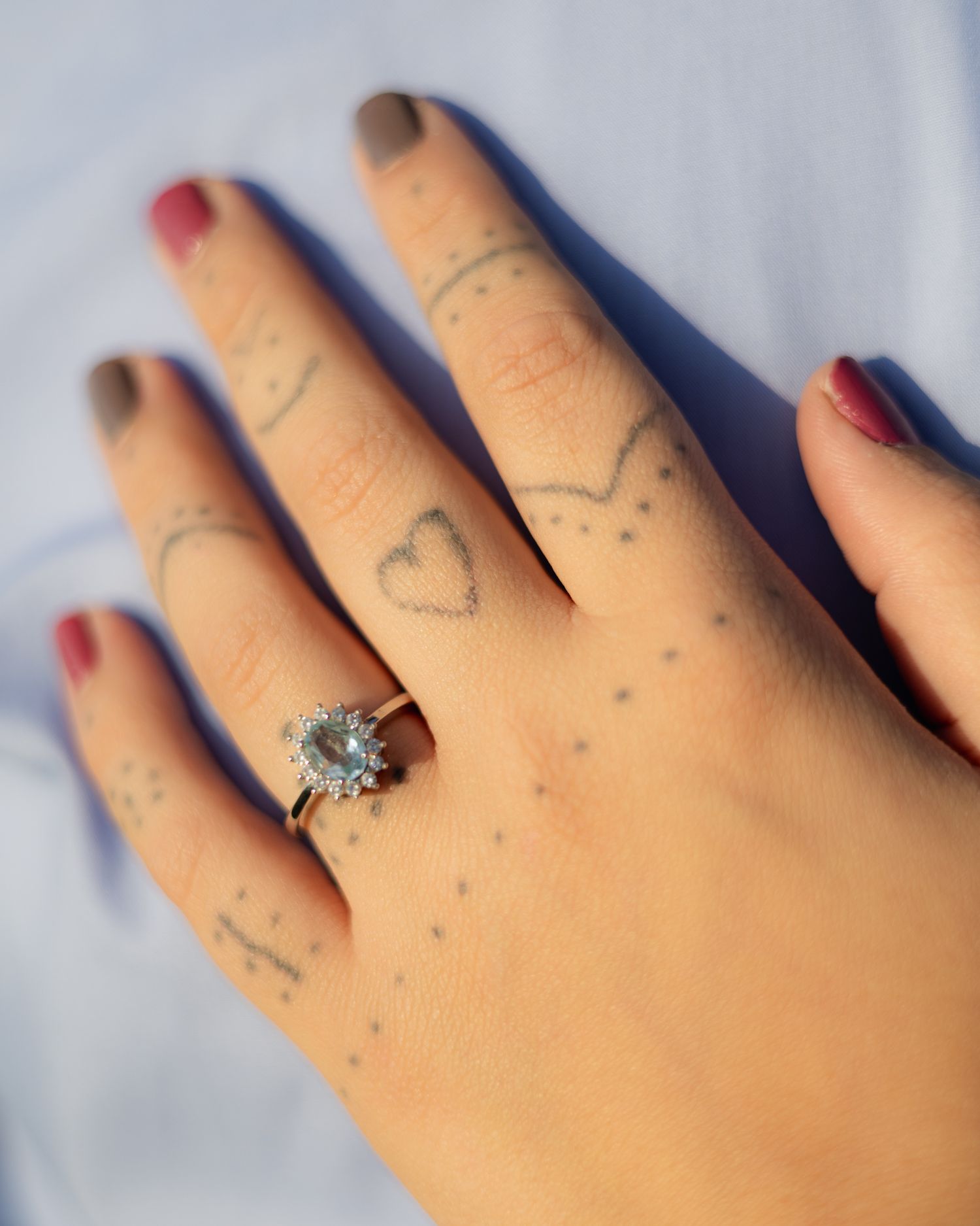 Hand with finger tattoos and heart designs wearing diamond halo engagement ring.