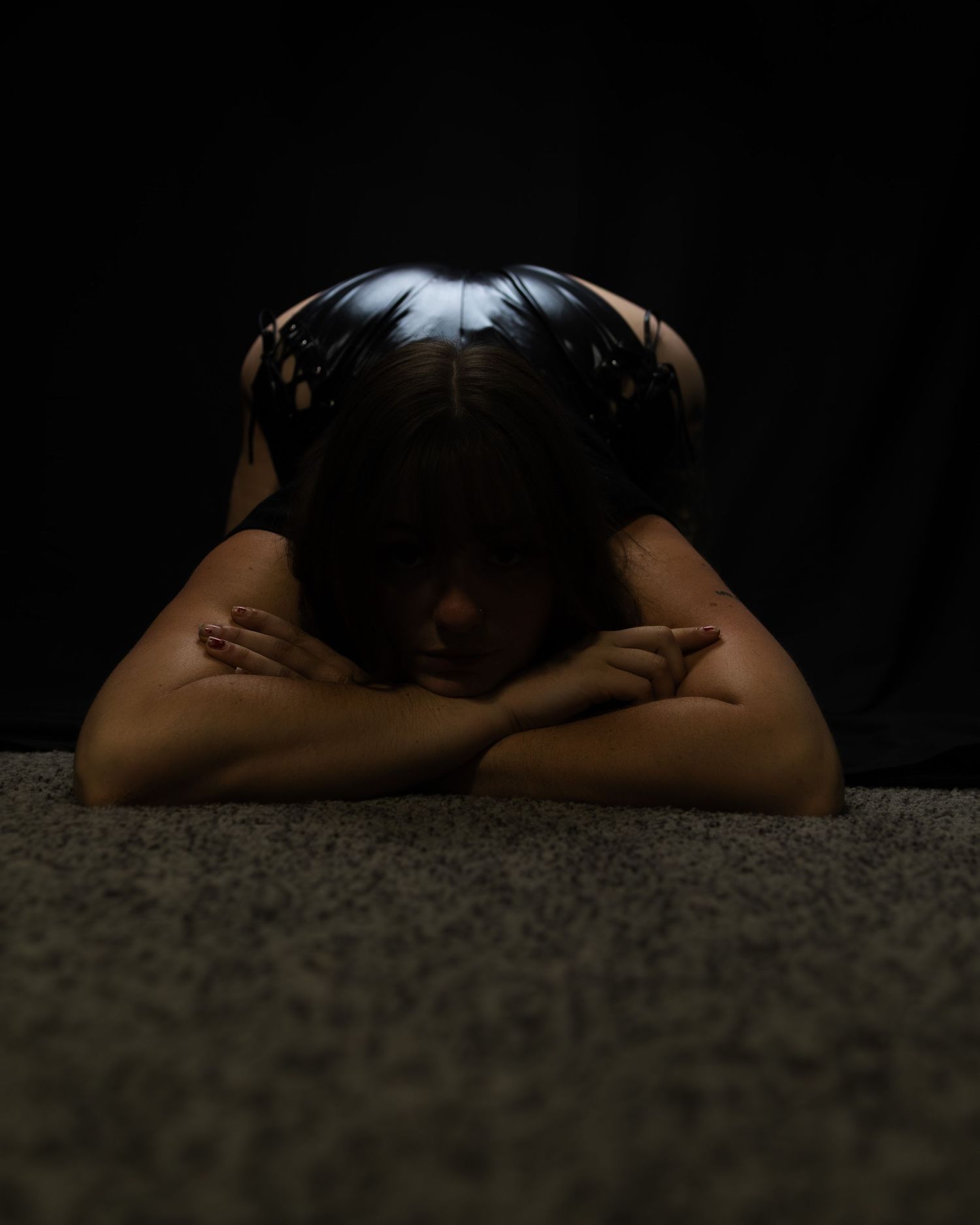 Person resting head on arms in a dramatic low-key dark studio portrait.