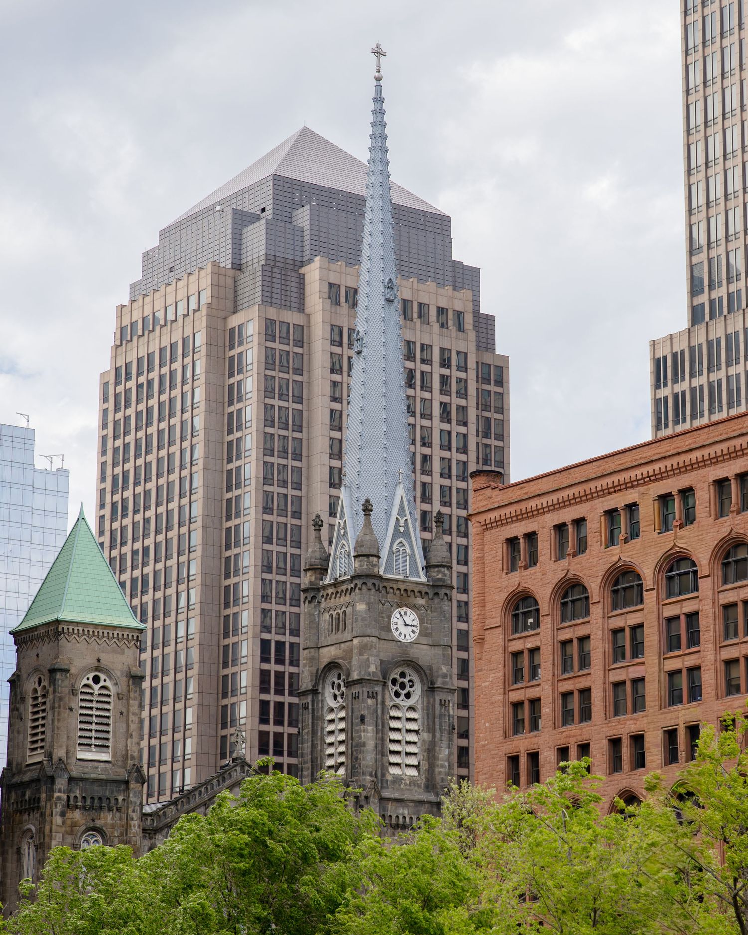 Historic church steeple with clock rises among modern skyscrapers and brick buildings in an urban downtown cityscape.