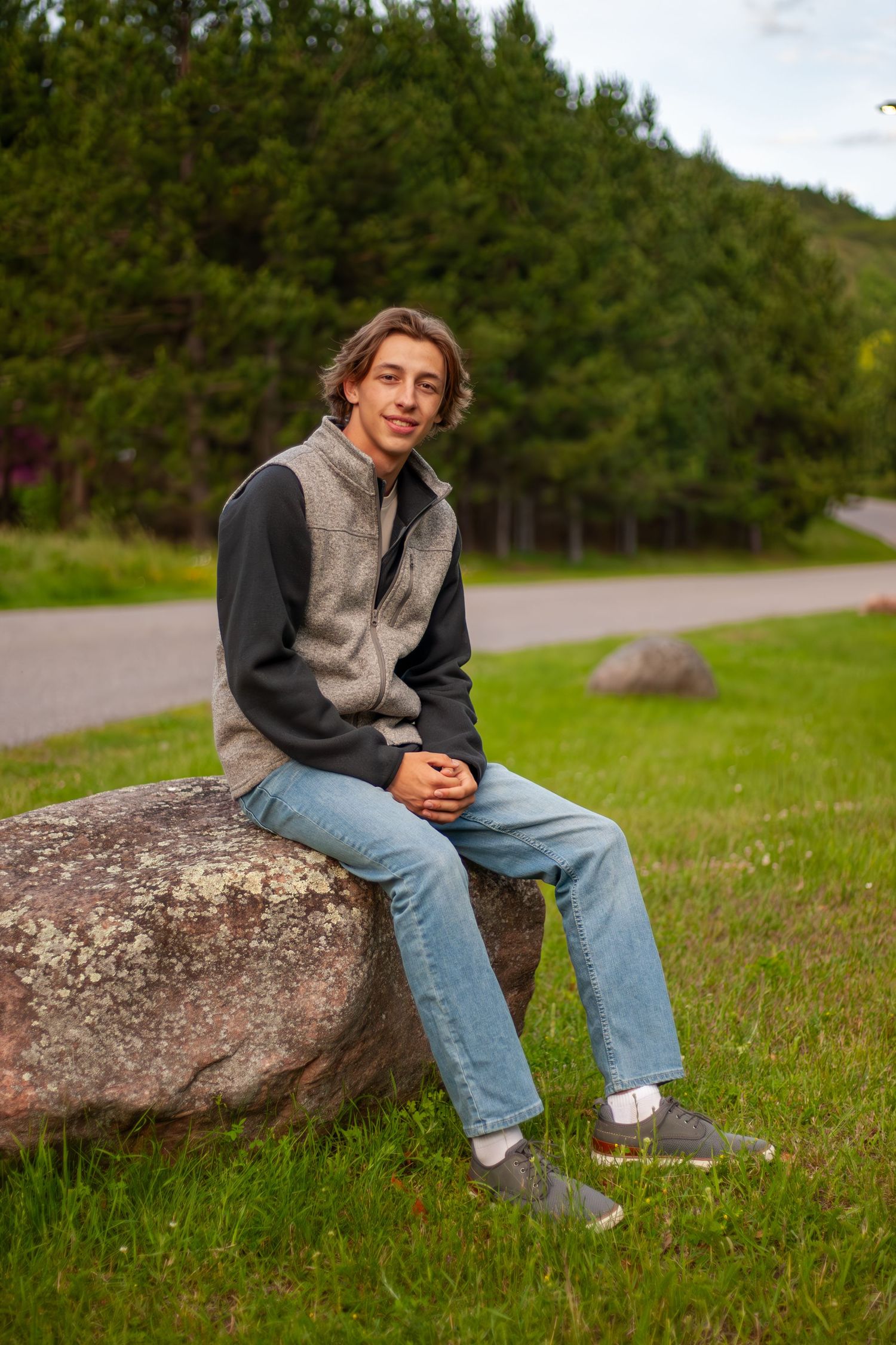 Casual portrait of person sitting on large rock with pine forest background.