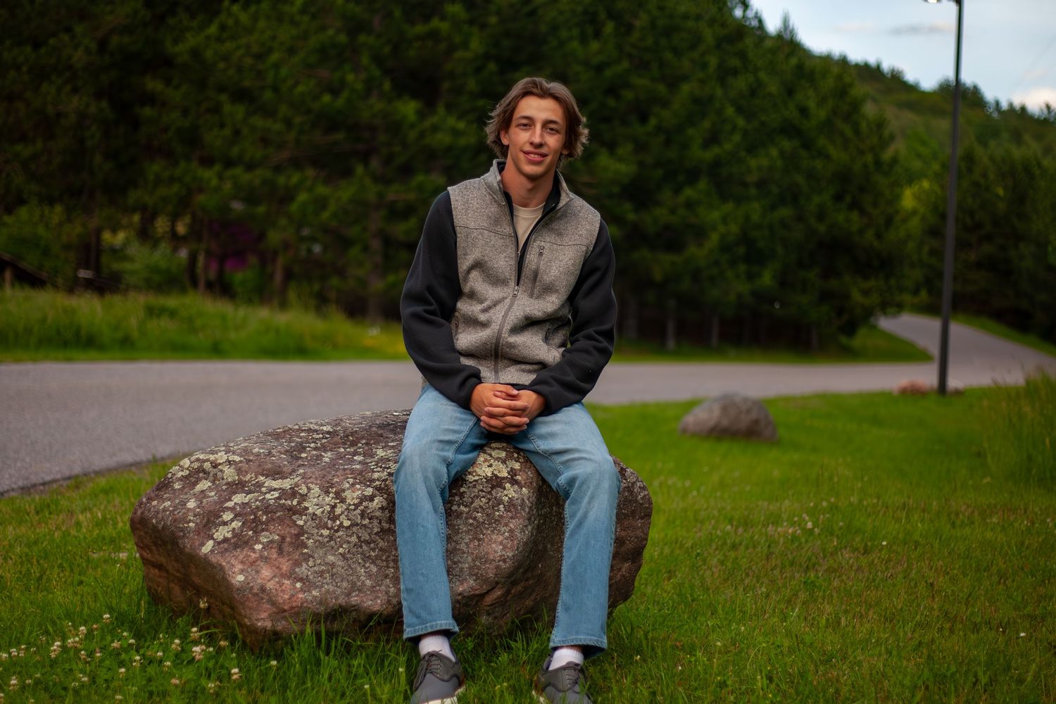 Person sitting casually on large rock in grassy outdoor setting during summer.