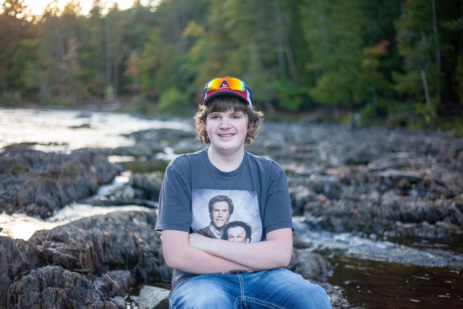 Person in baseball cap poses by rocky riverbed during sunset.