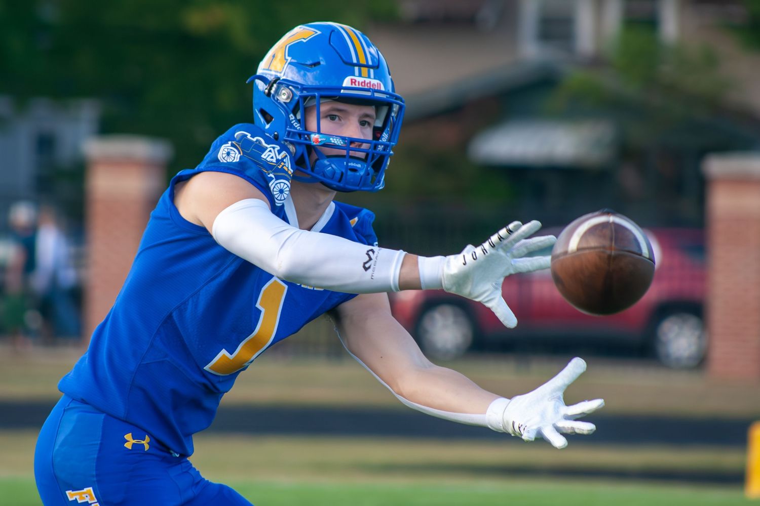 Football receiver in blue uniform extends to make diving catch during game.